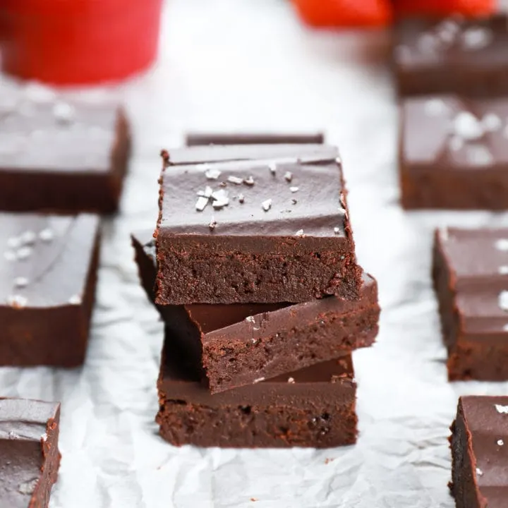 Stack of fudgy flourless brownies on a piece of parchment paper with a colander of strawberries in the background. Recipe from A Kitchen Addiction