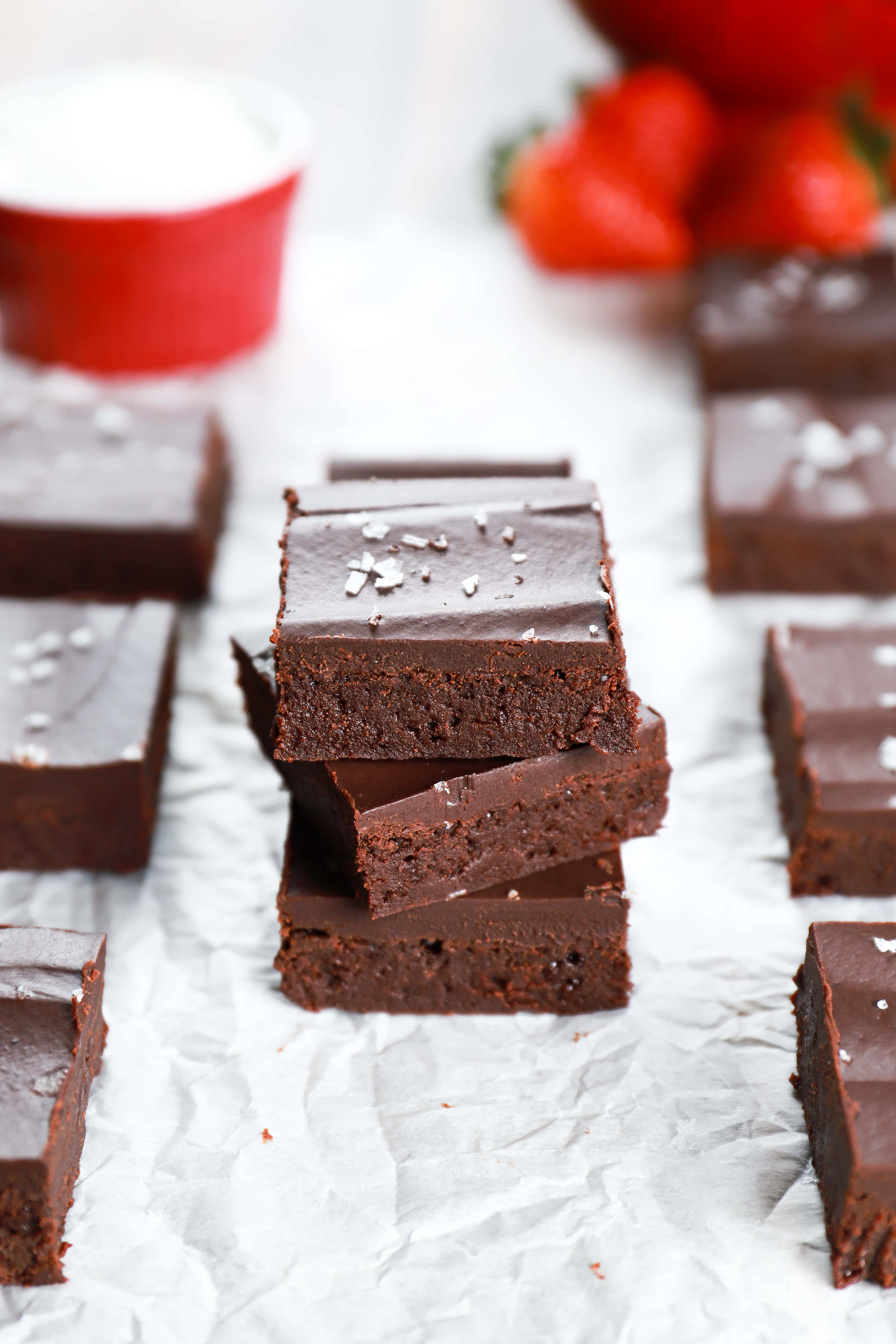 Stack of fudgy flourless brownies on a piece of parchment paper with a colander of strawberries in the background. Recipe from A Kitchen Addiction