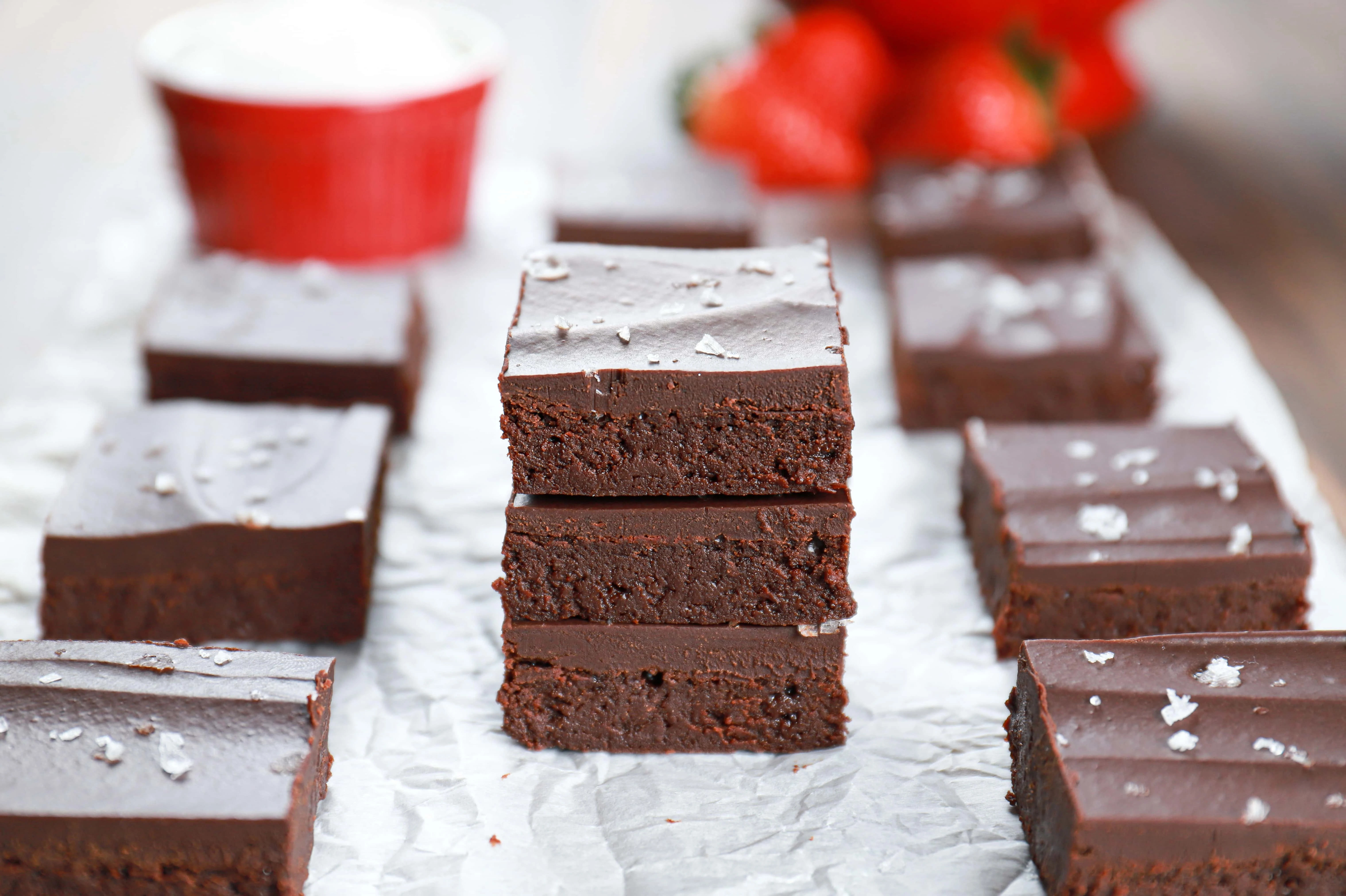 Three sea salt ganache topped flourless brownies stacked on a piece of parchment paper. Recipe from A Kitchen Addiction