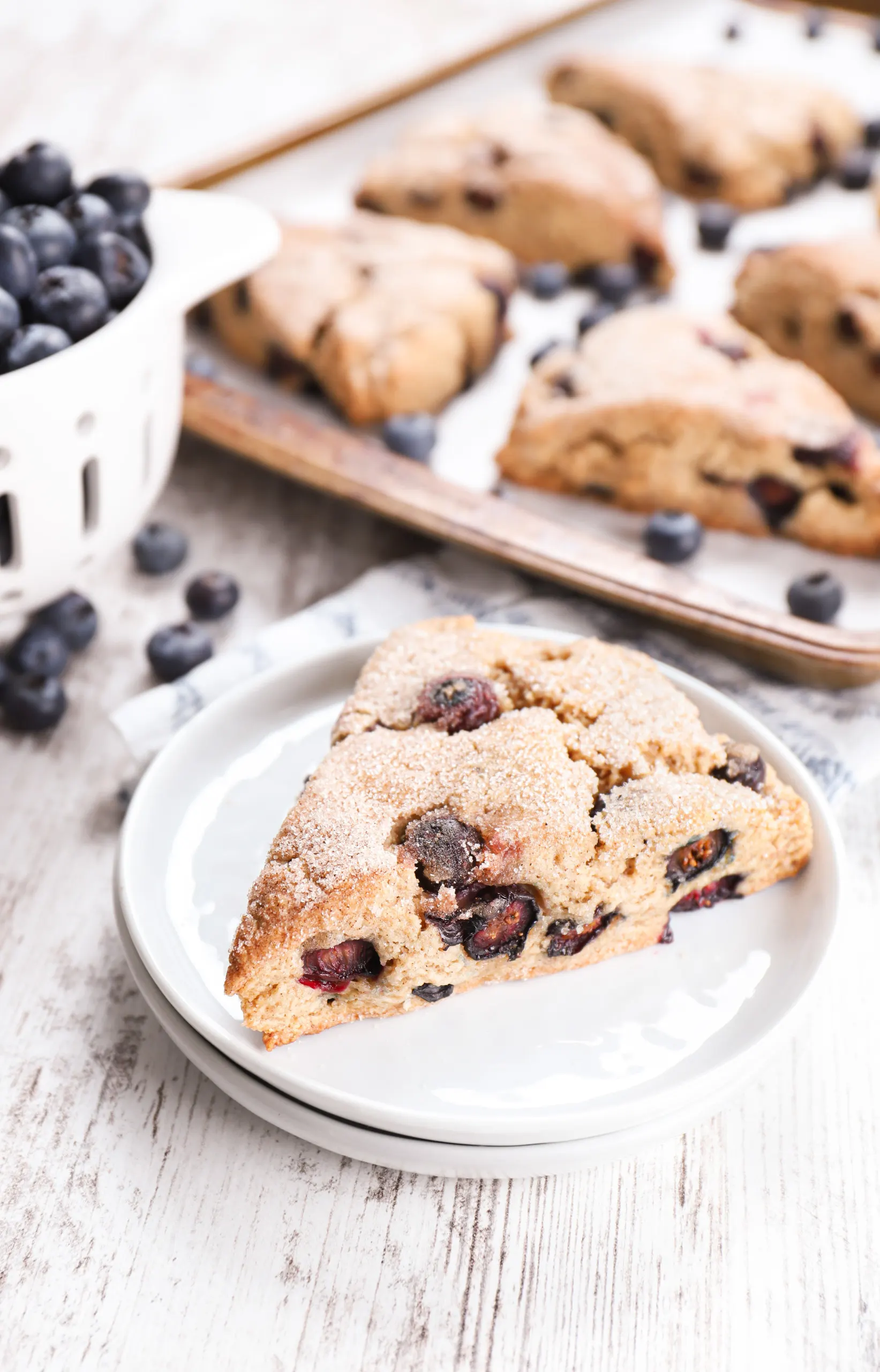 A blueberry snickerdoodle scones on a small white plate with remaining scones in the background.