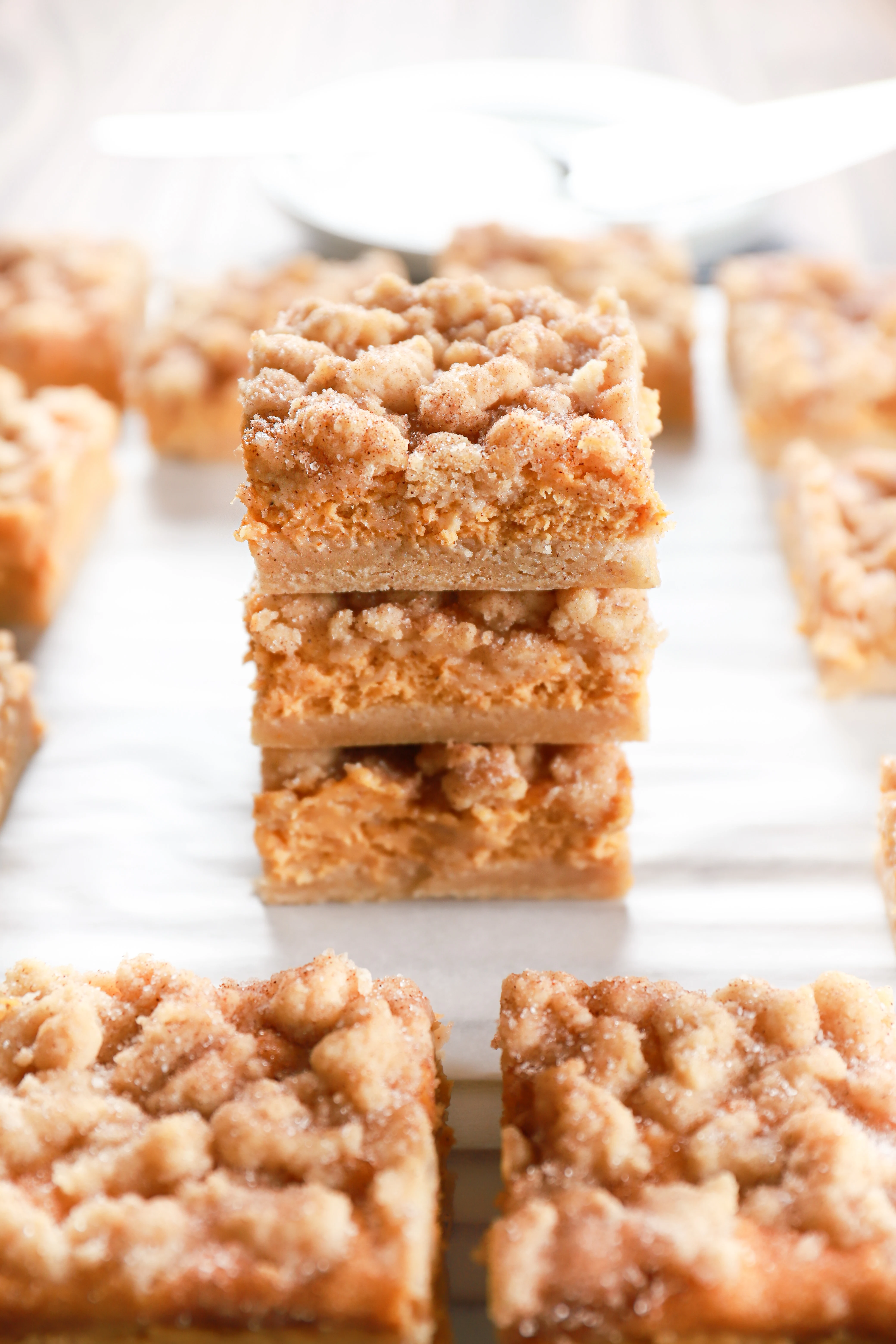 A stack of three pumpkin snickerdoodle cheesecake bars on a piece of parchment paper.