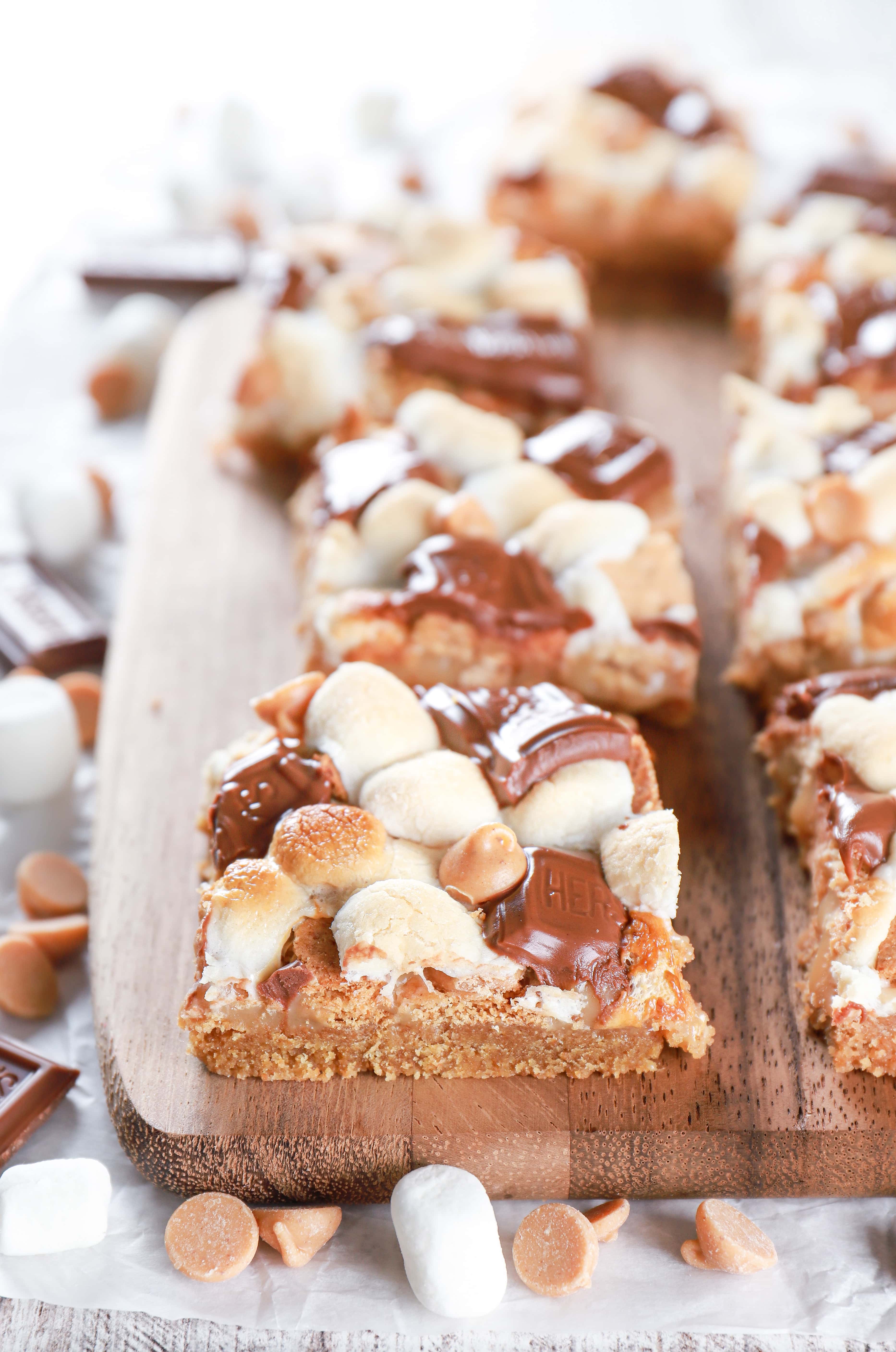 Side view of a peanut butter smores seven layer bar on a wooden cutting board. Recipe from A Kitchen Addiction