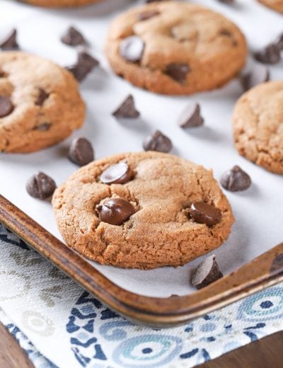 Up close image of a flourless almond butter chocolate chip cookie on a parchment paper covered cookie sheet. Recipe from A Kitchen Addiction