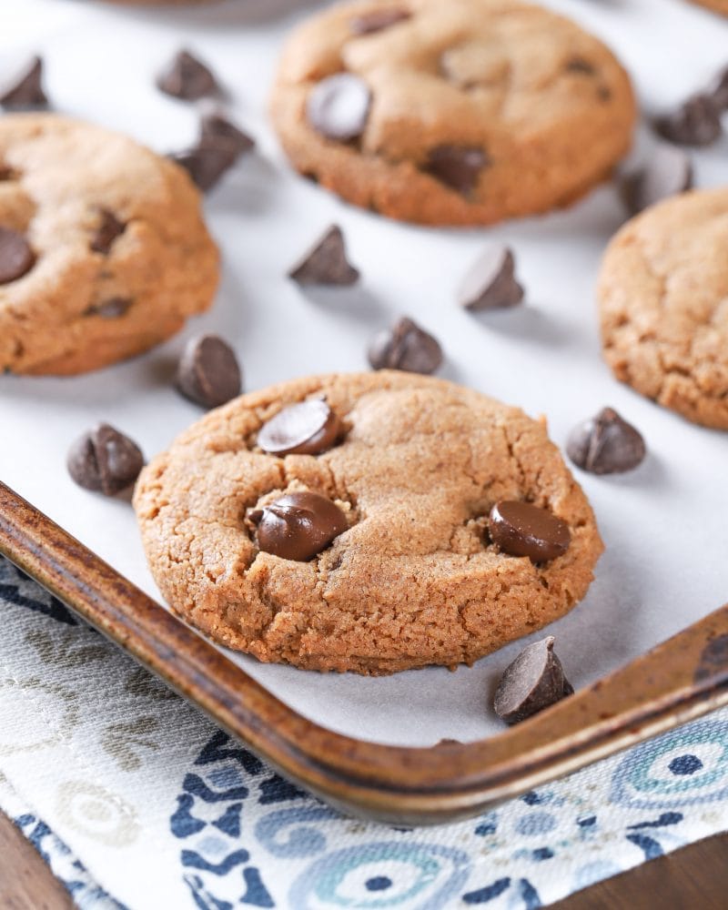 Up close image of a flourless almond butter chocolate chip cookie on a parchment paper covered cookie sheet. Recipe from A Kitchen Addiction