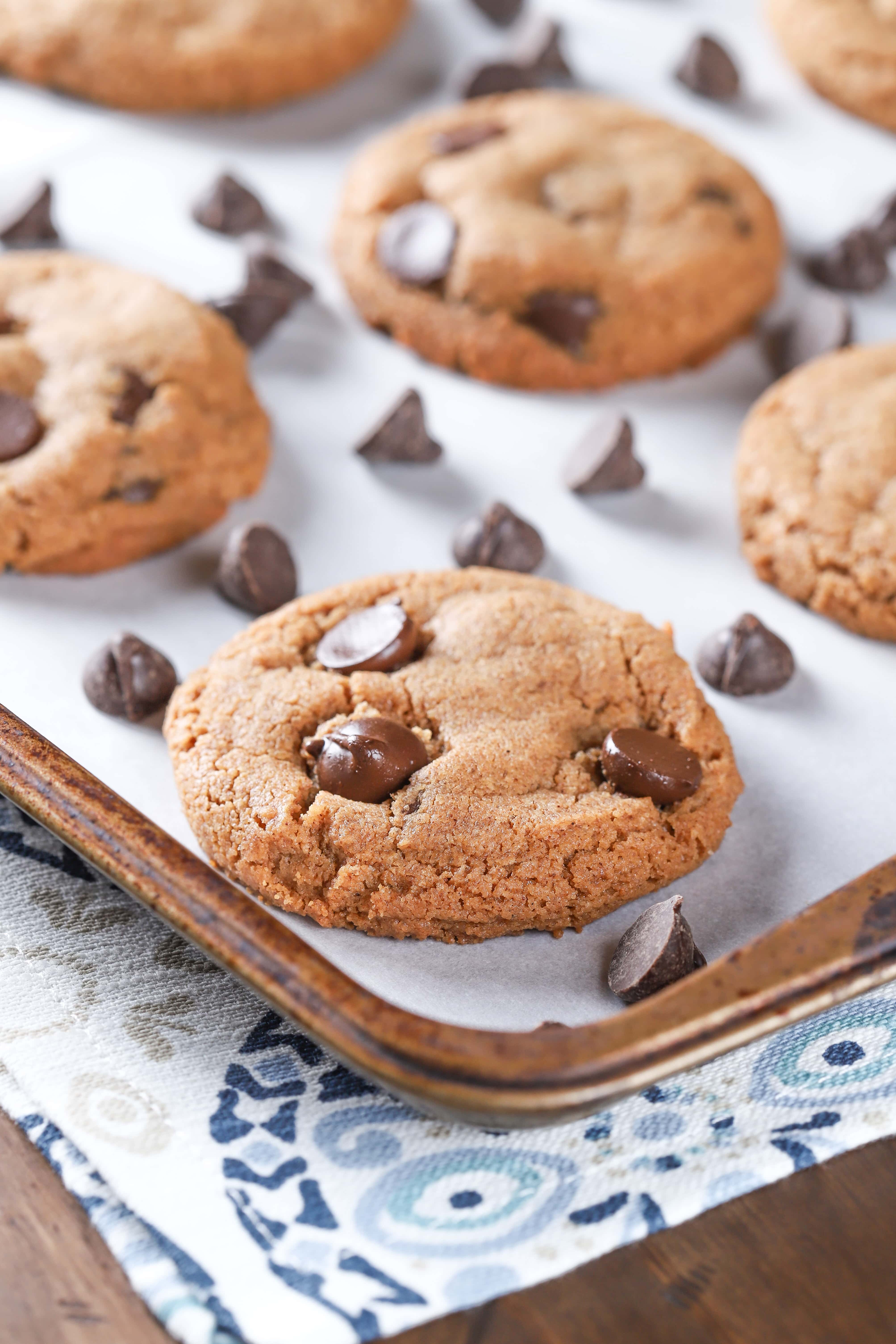 Up close image of a flourless almond butter chocolate chip cookie on a parchment paper covered cookie sheet. Recipe from A Kitchen Addiction