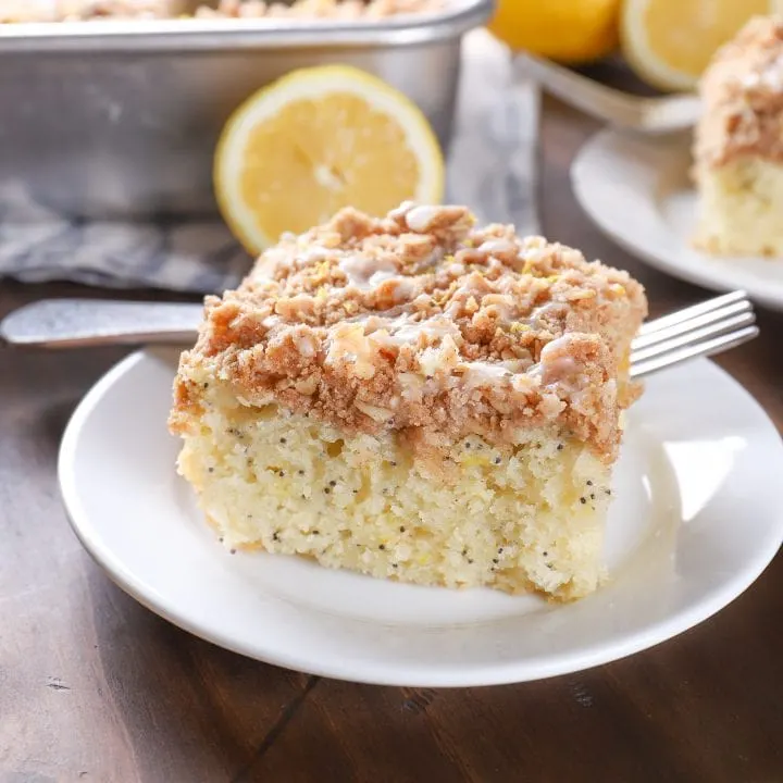 Up close image of a piece of lemon poppy seed cake on a white plate with a pan of cake in the background.