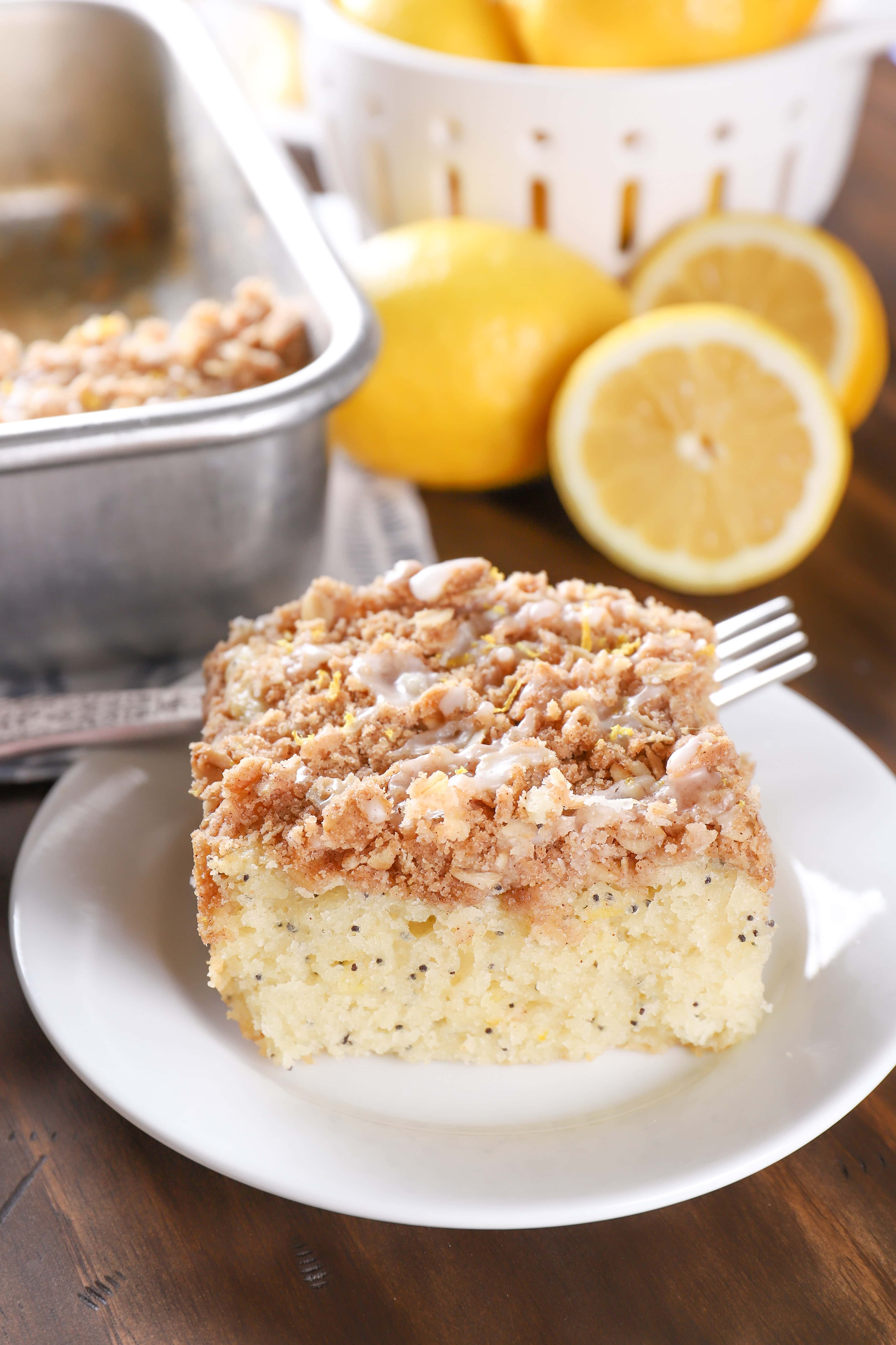 Piece of lemon poppy seed coffee cake on a white plate with lemons in the background. Recipe from A Kitchen Addiction