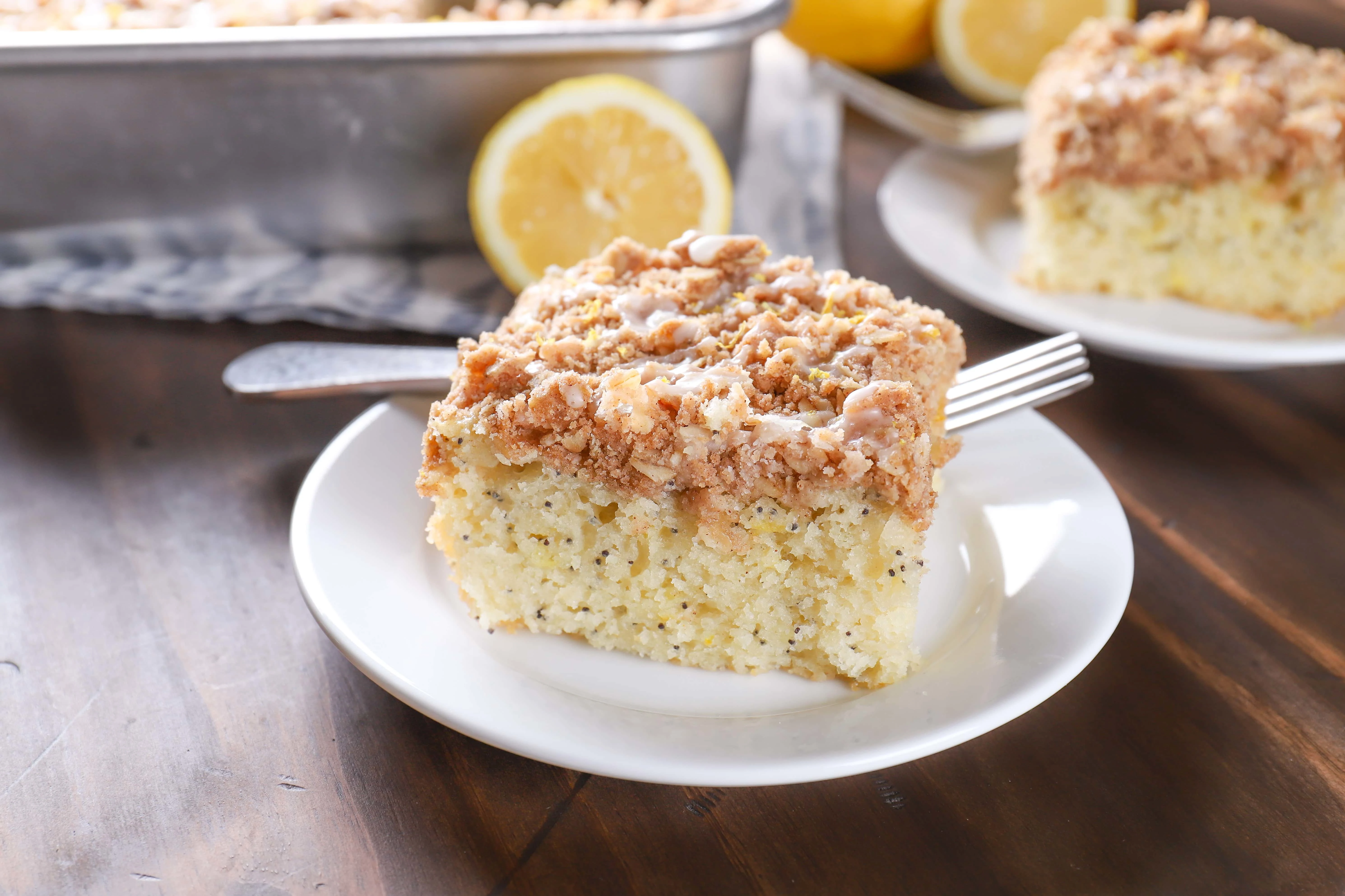 Up close image of a piece of lemon poppy seed cake on a white plate with a pan of cake in the background.