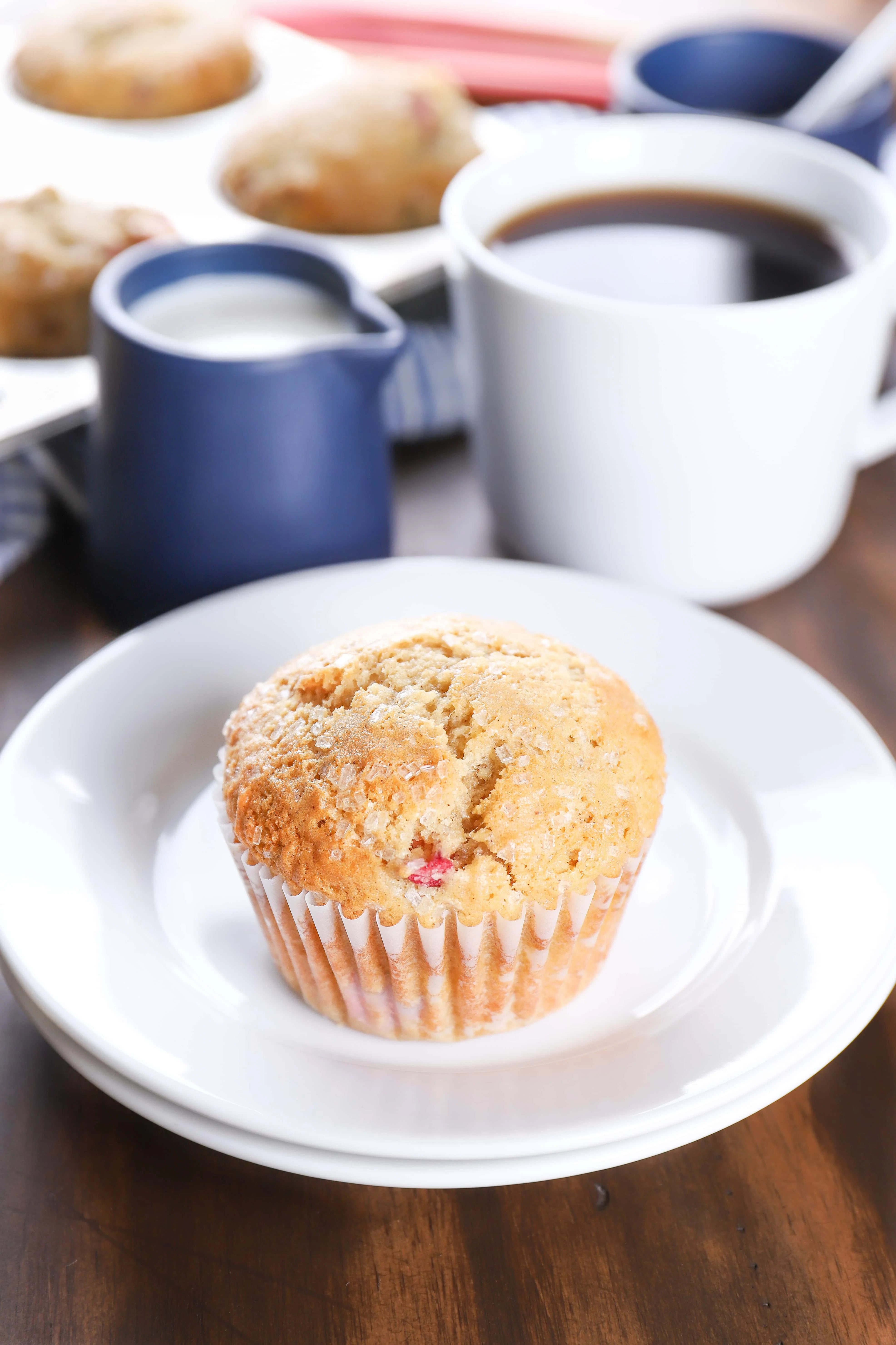 A bakery style rhubarb muffin on a plate with a cup of coffee. Recipe from A Kitchen Addiction