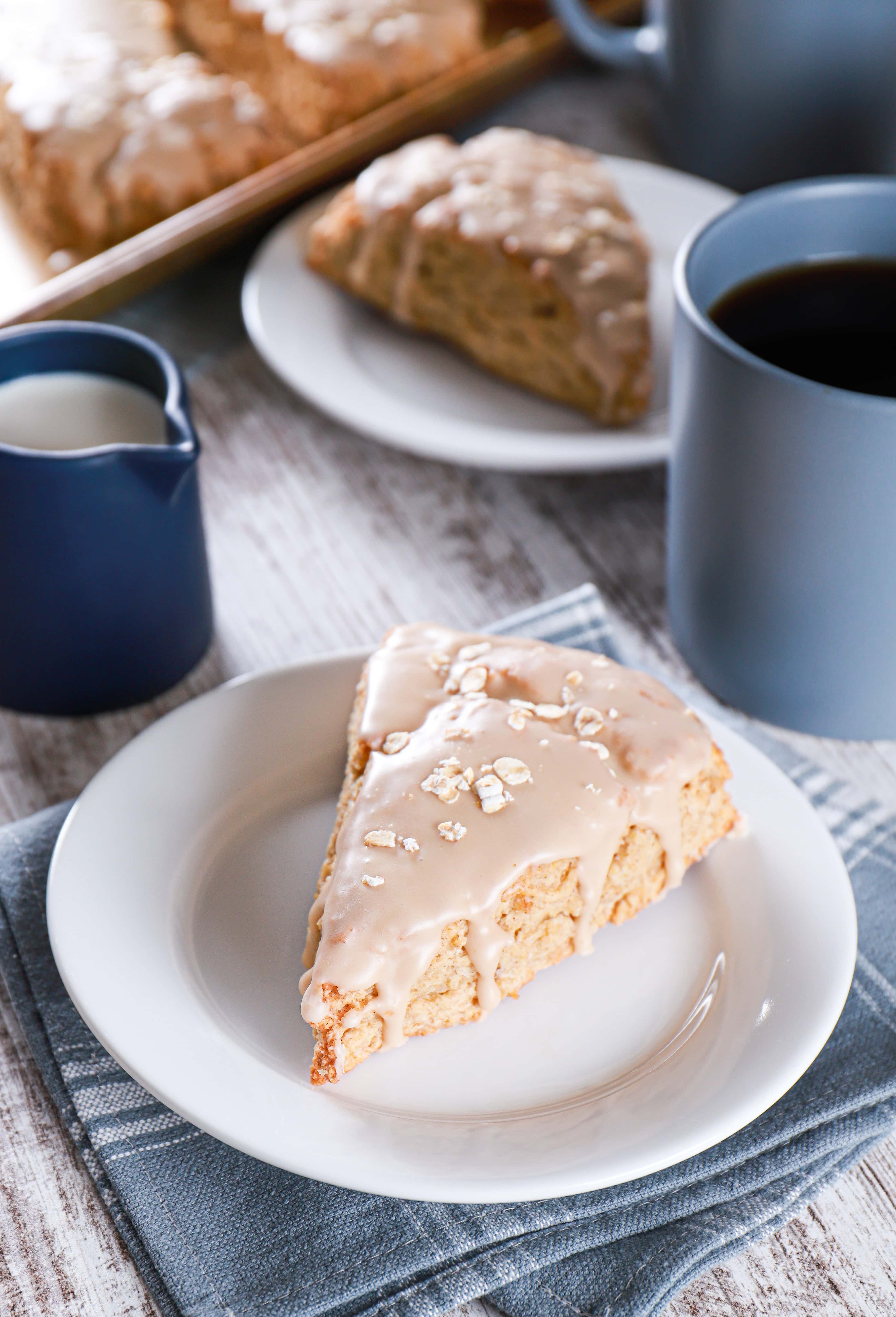 Maple oat scone on a white plate with coffee and scones in the background. Recipe from A Kitchen Addiction