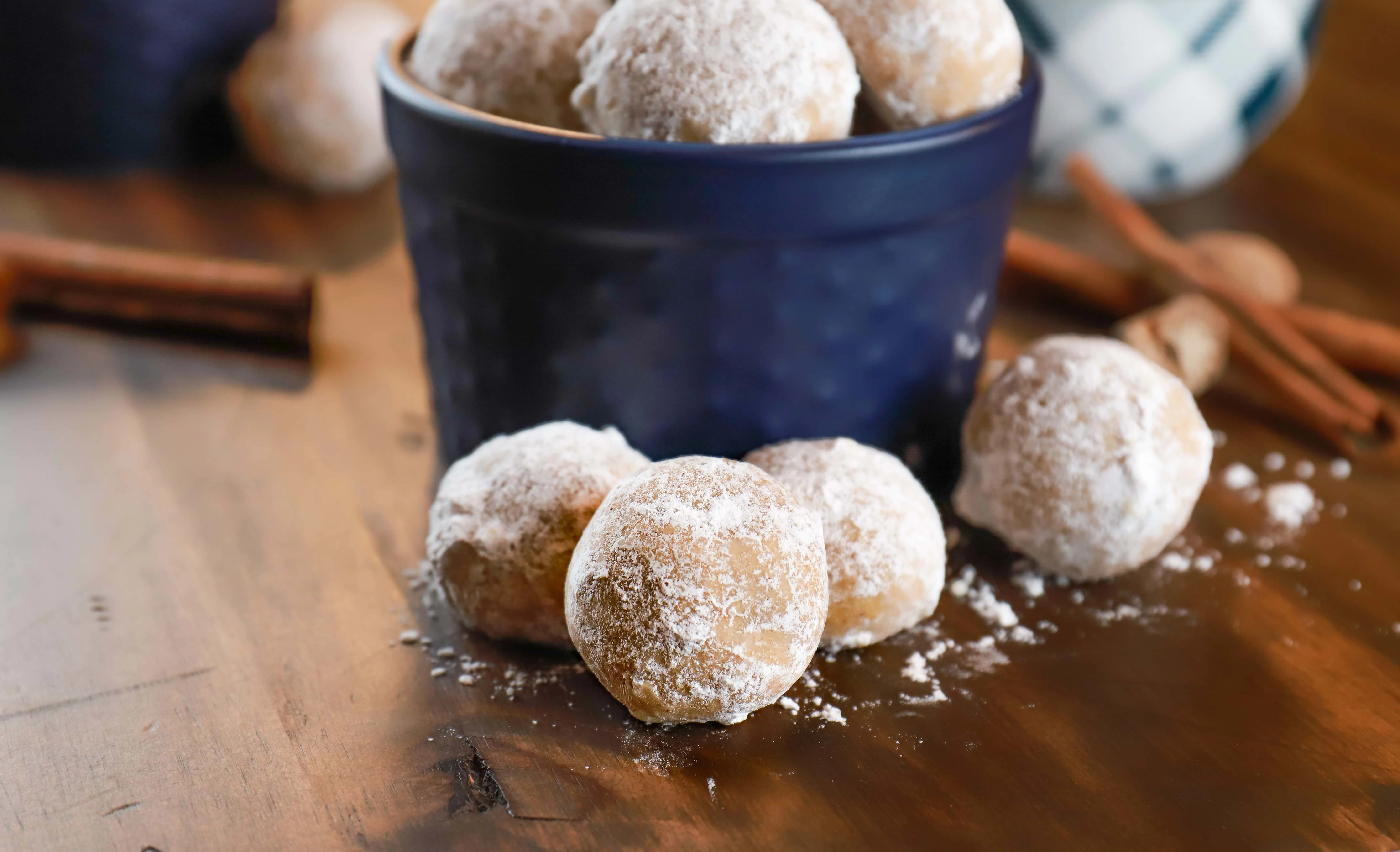 Up close image of gingerbread snowball cookies in front of a blue dish holding more gingerbread snowball cookies. Recipe from A Kitchen Addiction