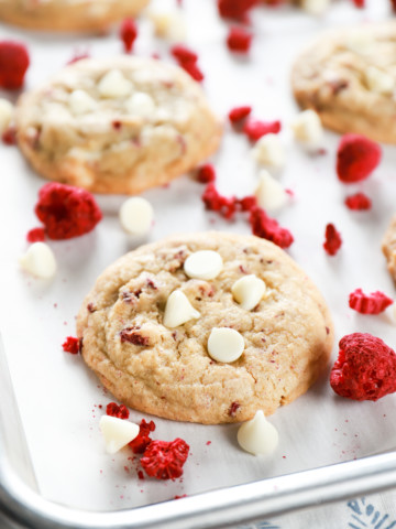 Up close image of a chewy white chocolate raspberry cookie on a parchment paper lined baking sheet. Recipe for cookies from A Kitchen Addiction