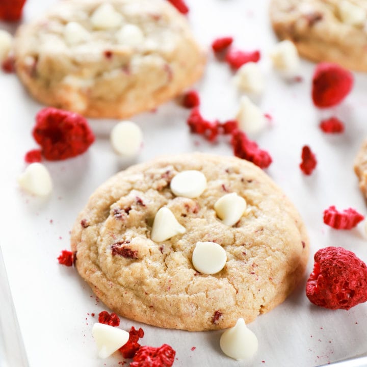 Up close image of a chewy white chocolate raspberry cookie on a parchment paper lined baking sheet. Recipe for cookies from A Kitchen Addiction