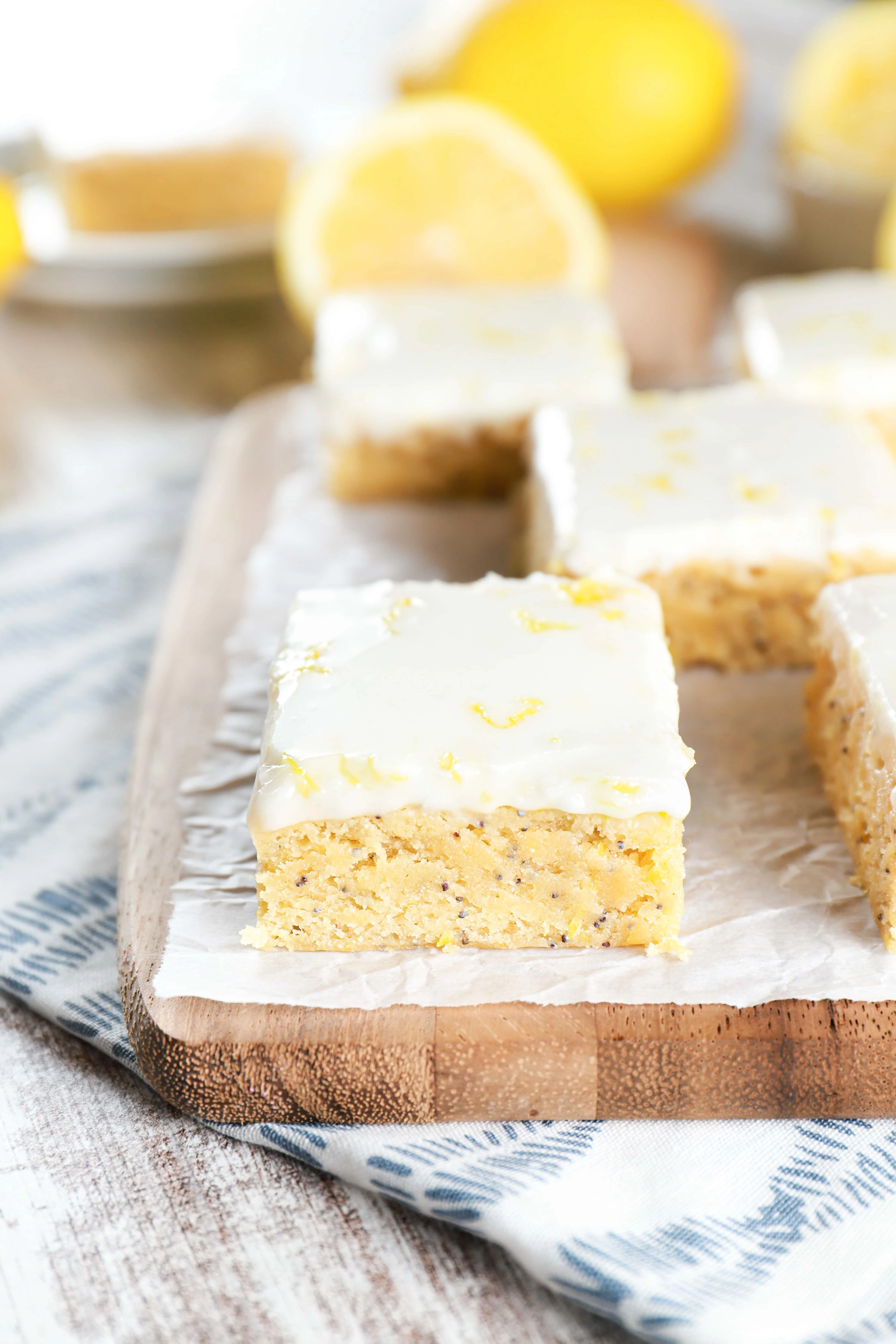 Up close image of glazed lemon poppy seed bars on a parchment paper lined cutting board. Recipe from A Kitchen Addiction