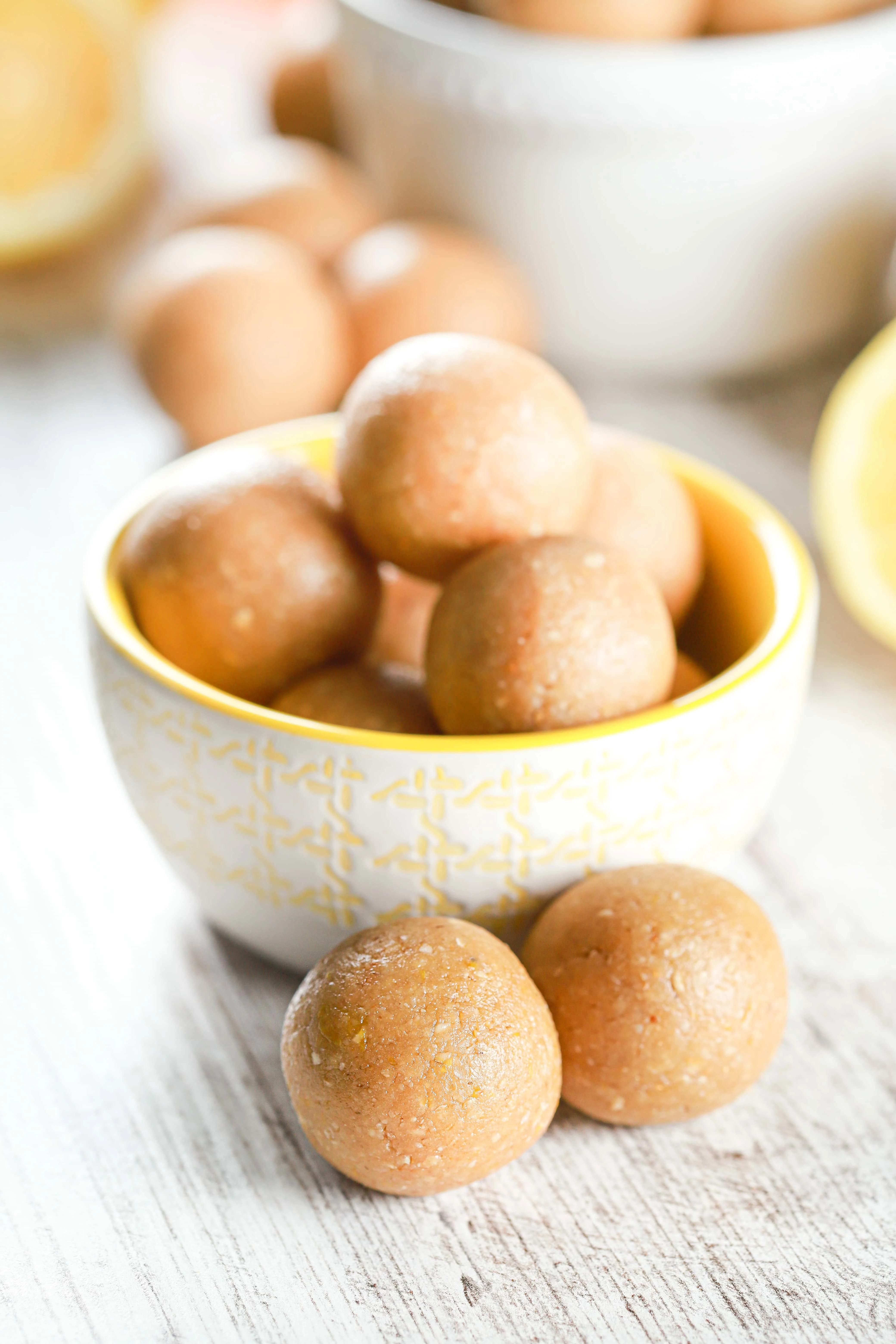 Lemon Protein Bites in a small yellow and white bowl with more bites in the background. Recipe for Lemon Protein Bites from A Kitchen Addiction