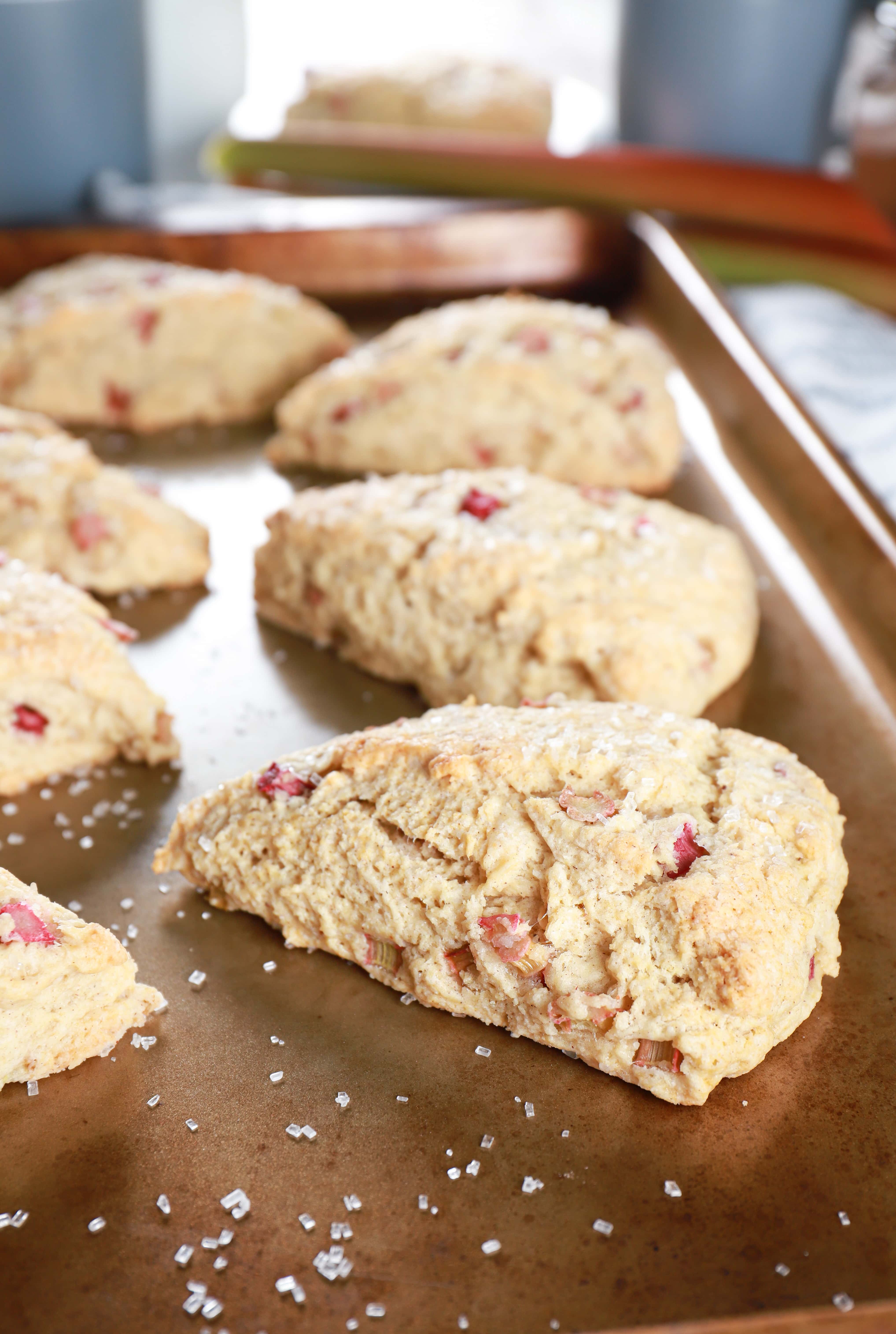 Side view of a rhubarb scone sitting on a baking sheet with more scones in the background. Recipe for scones from A Kitchen Addiction