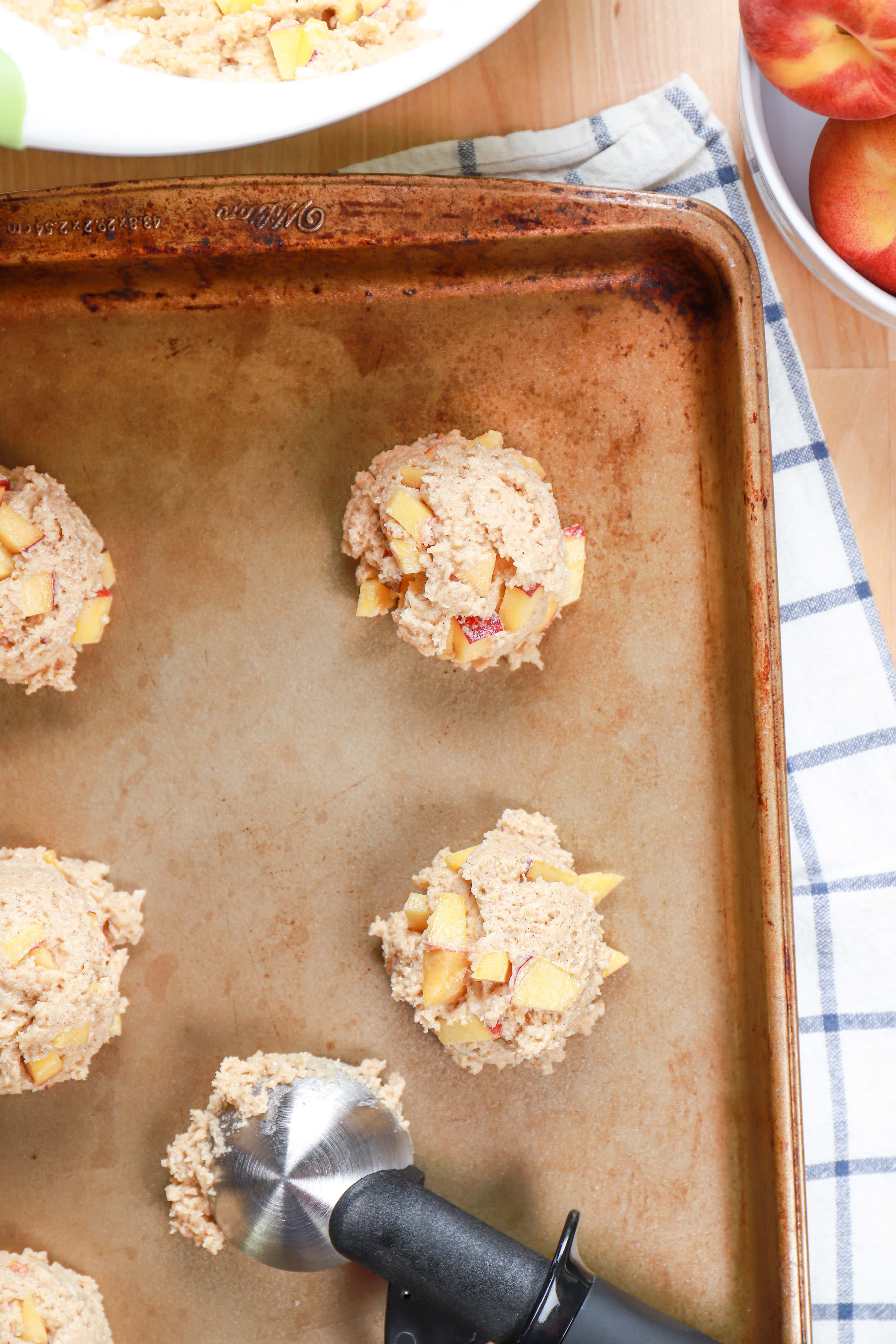 Peach fritter dough scooped out with a ice cream scoop on a baking sheet.