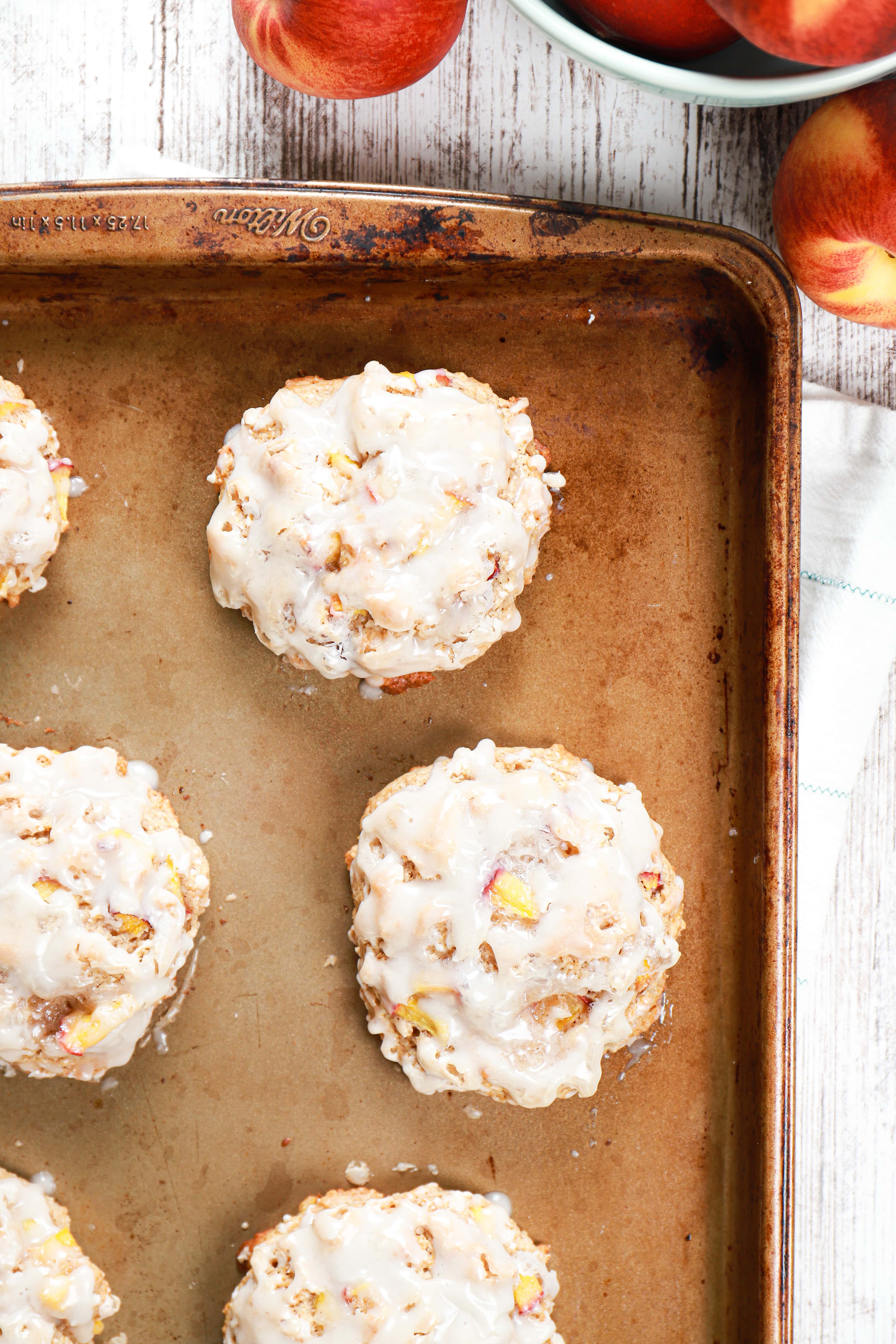 Overhead view of baked peach fritters on a baking sheet with a bowl of peaches beside the baking sheet.