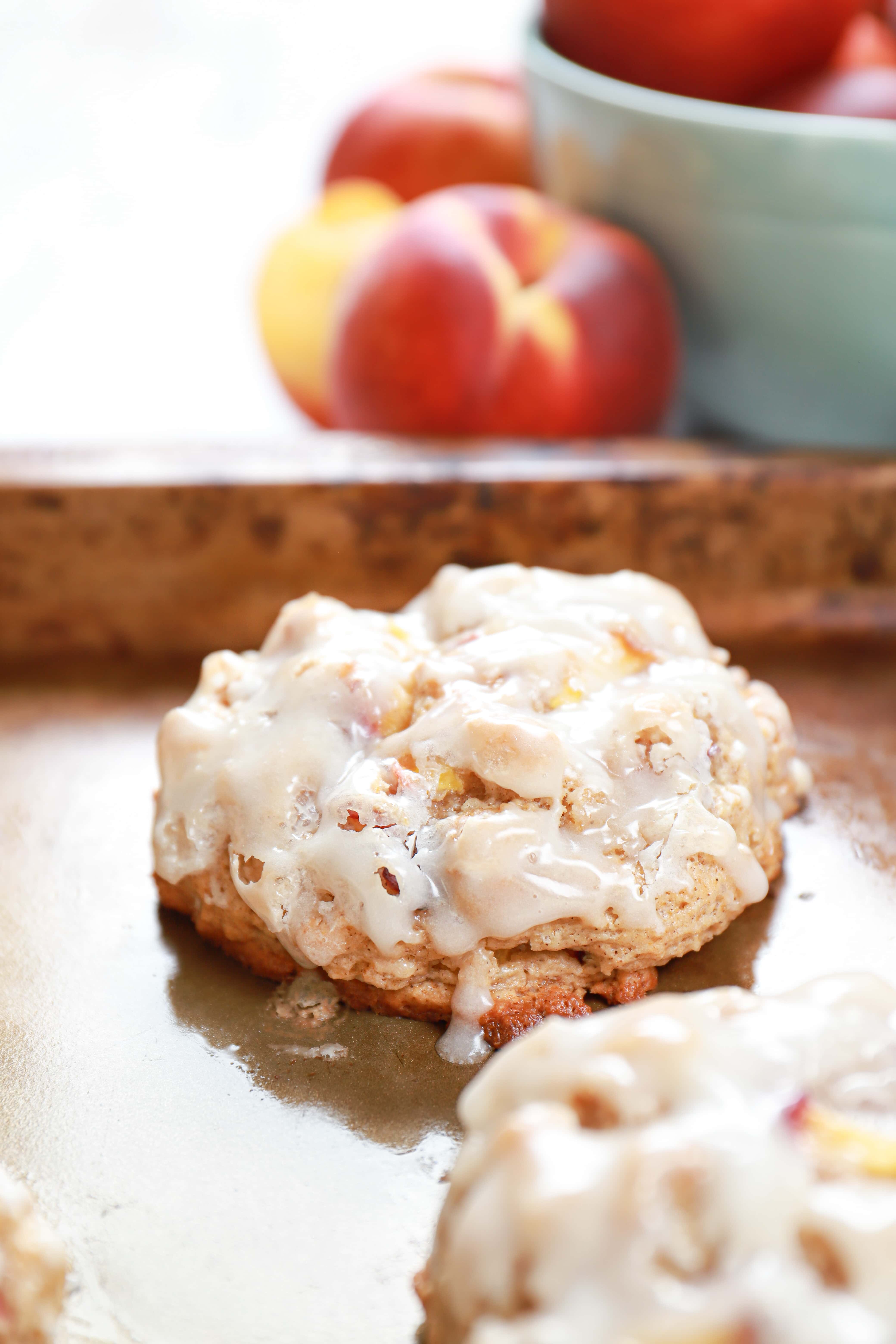 Up close image of a baked peach fritter on a baking sheet with peaches in the background.