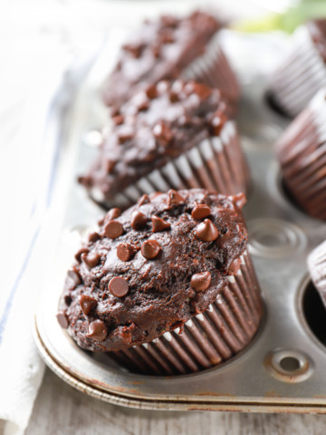Double Chocolate Zucchini Muffins in a silver muffin tin with zucchini in the background