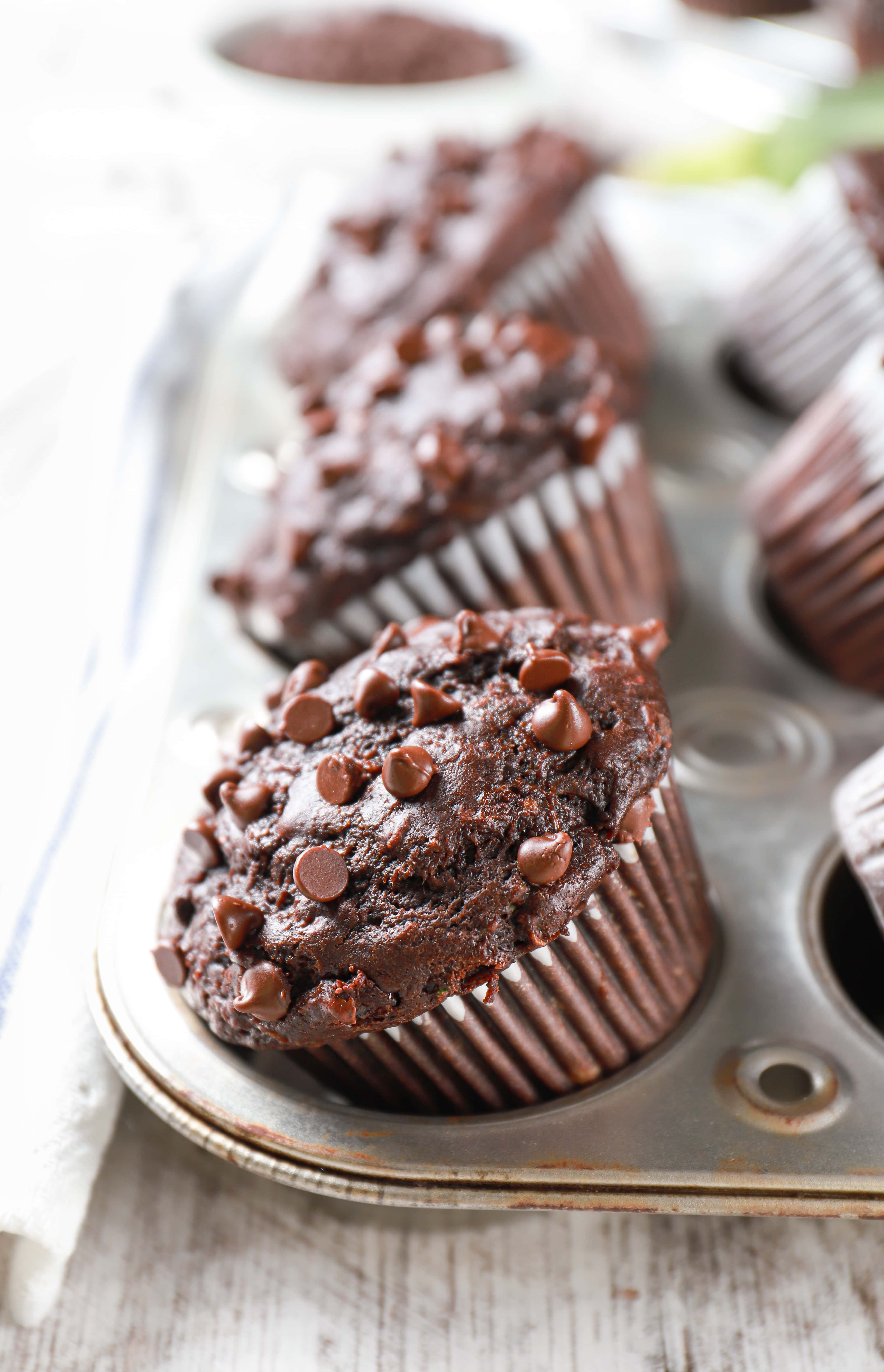 Double Chocolate Zucchini Muffins in a silver muffin tin with zucchini in the background