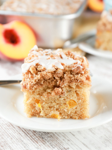 Side view of a piece of peach coffee cake with baking dish of peach coffee cake in the background.