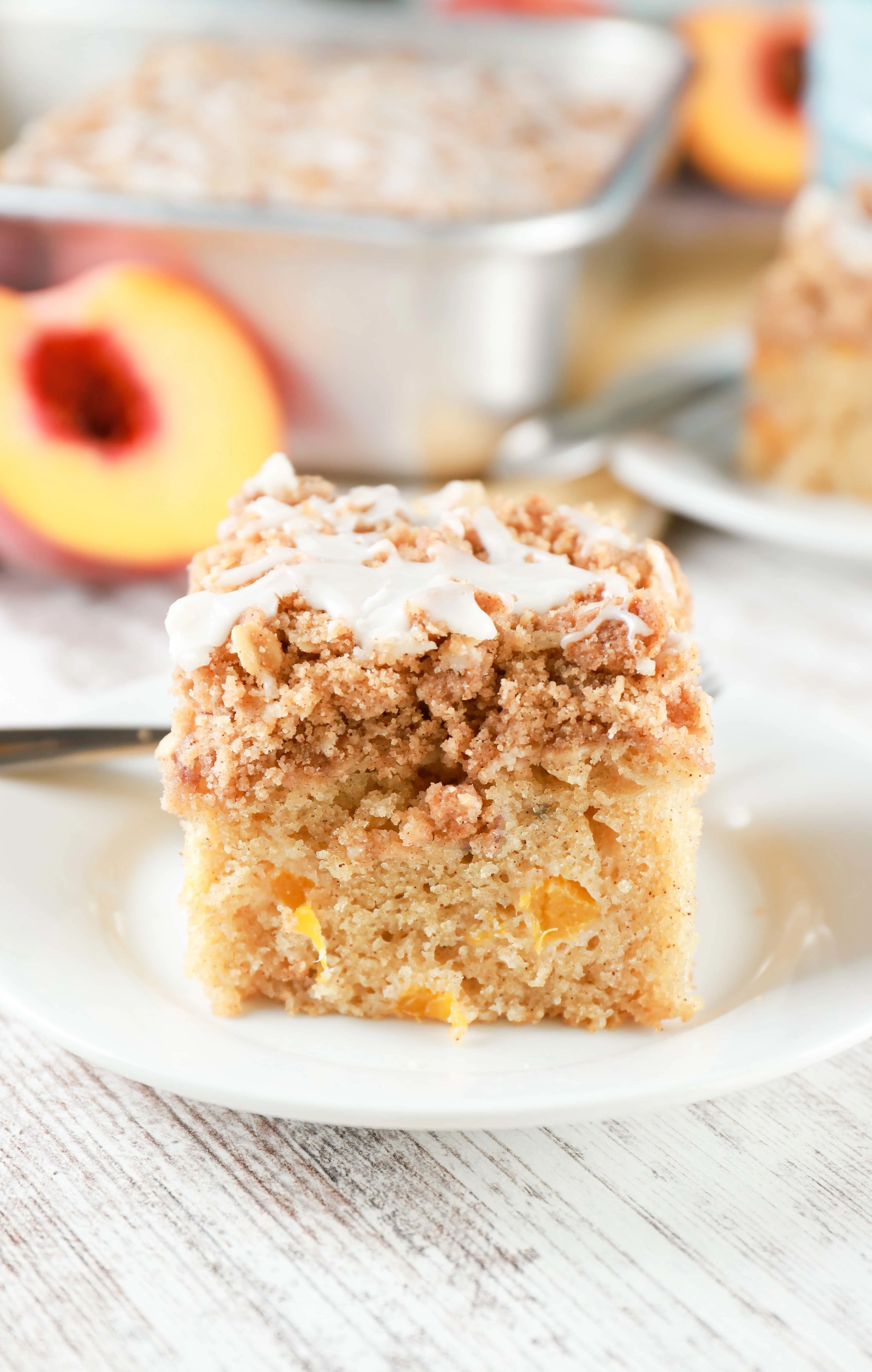 Side view of a piece of peach coffee cake with baking dish of peach coffee cake in the background.