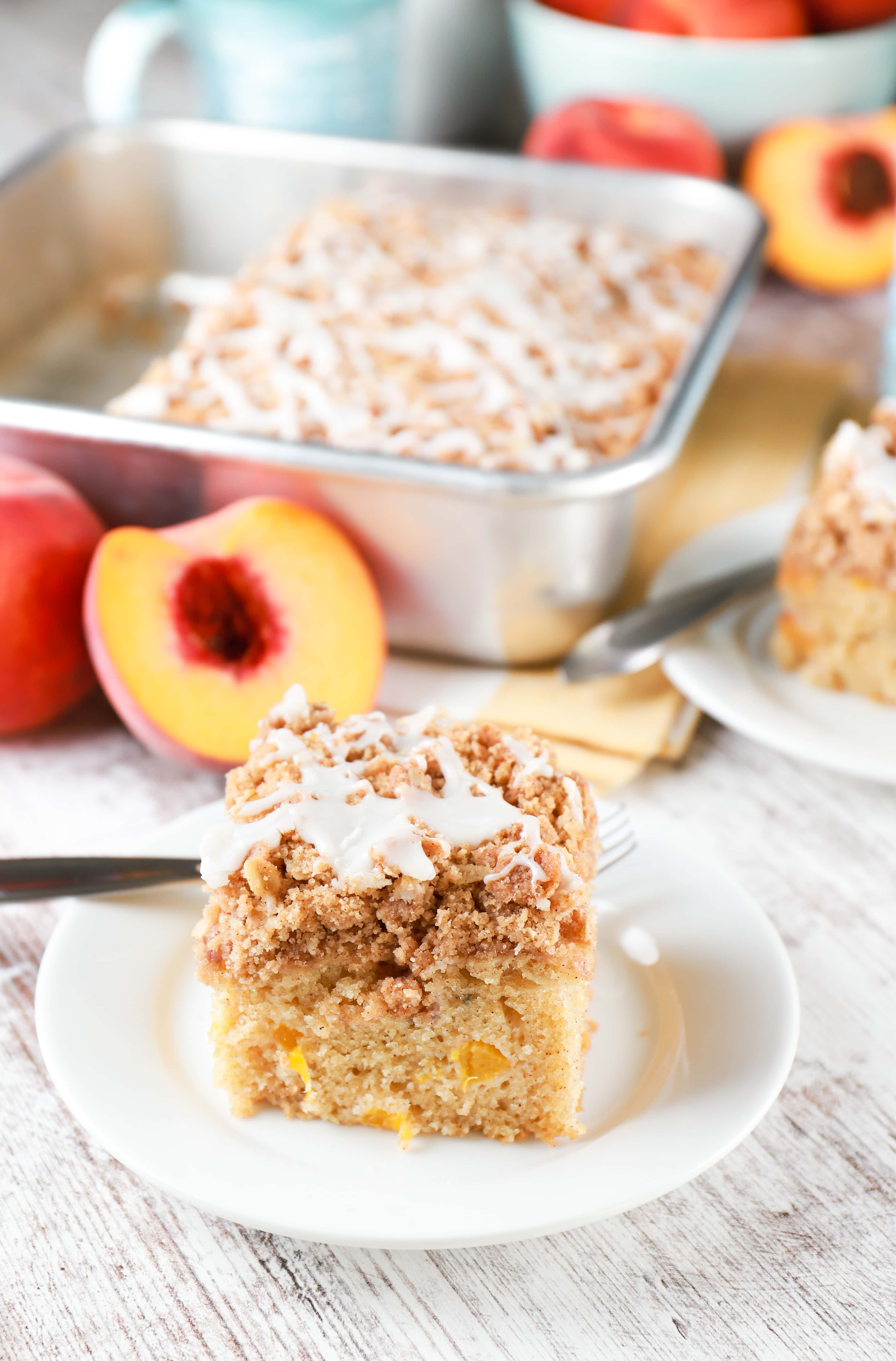Two slices of peach coffee cake on small white plates with pan of remaining cake in the background.