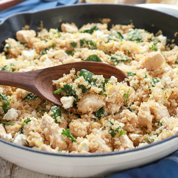 wooden spoon with a scoop of lemon feta chicken quinoa skillet in a white cast iron skillet