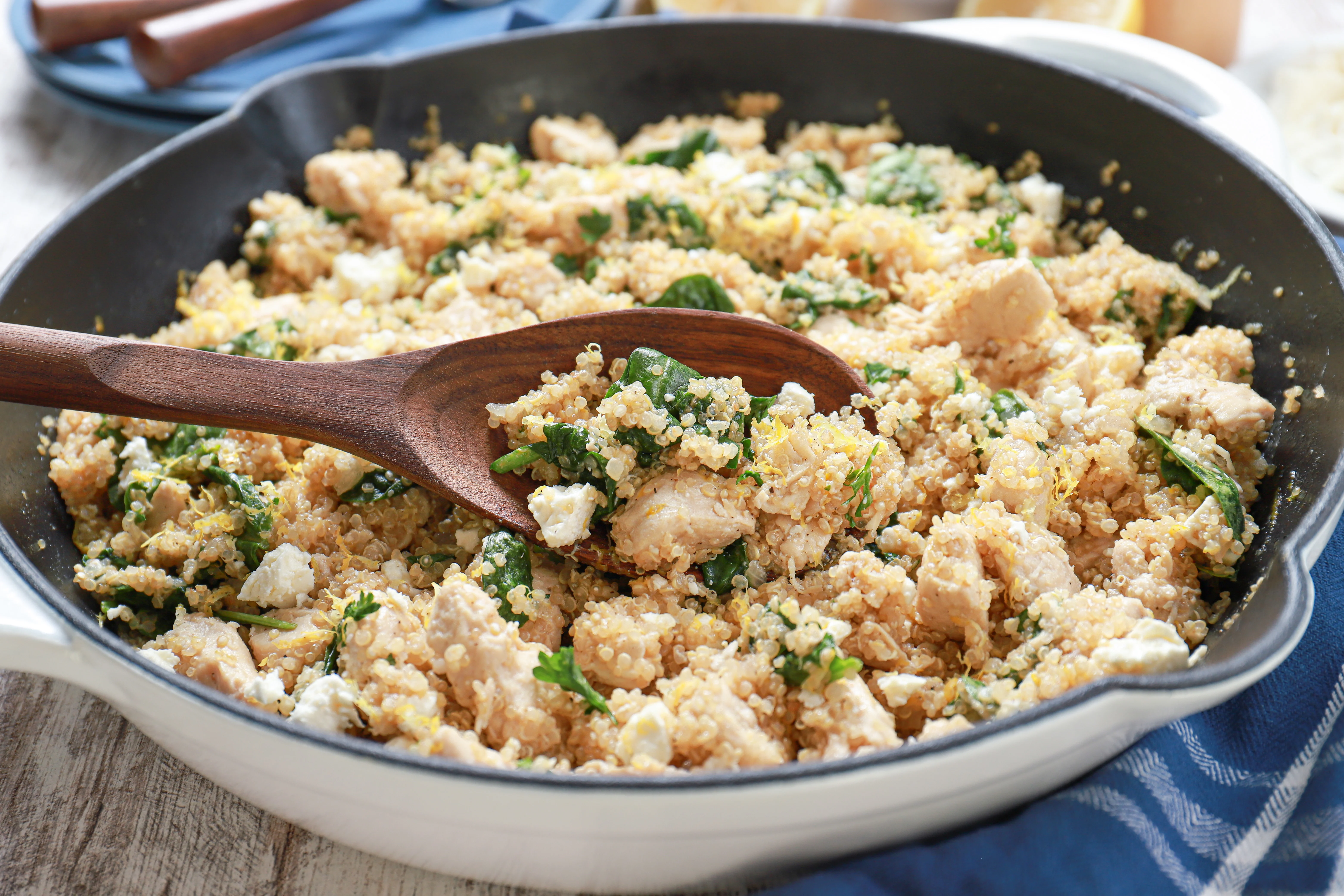 wooden spoon with a scoop of lemon feta chicken quinoa skillet in a white cast iron skillet