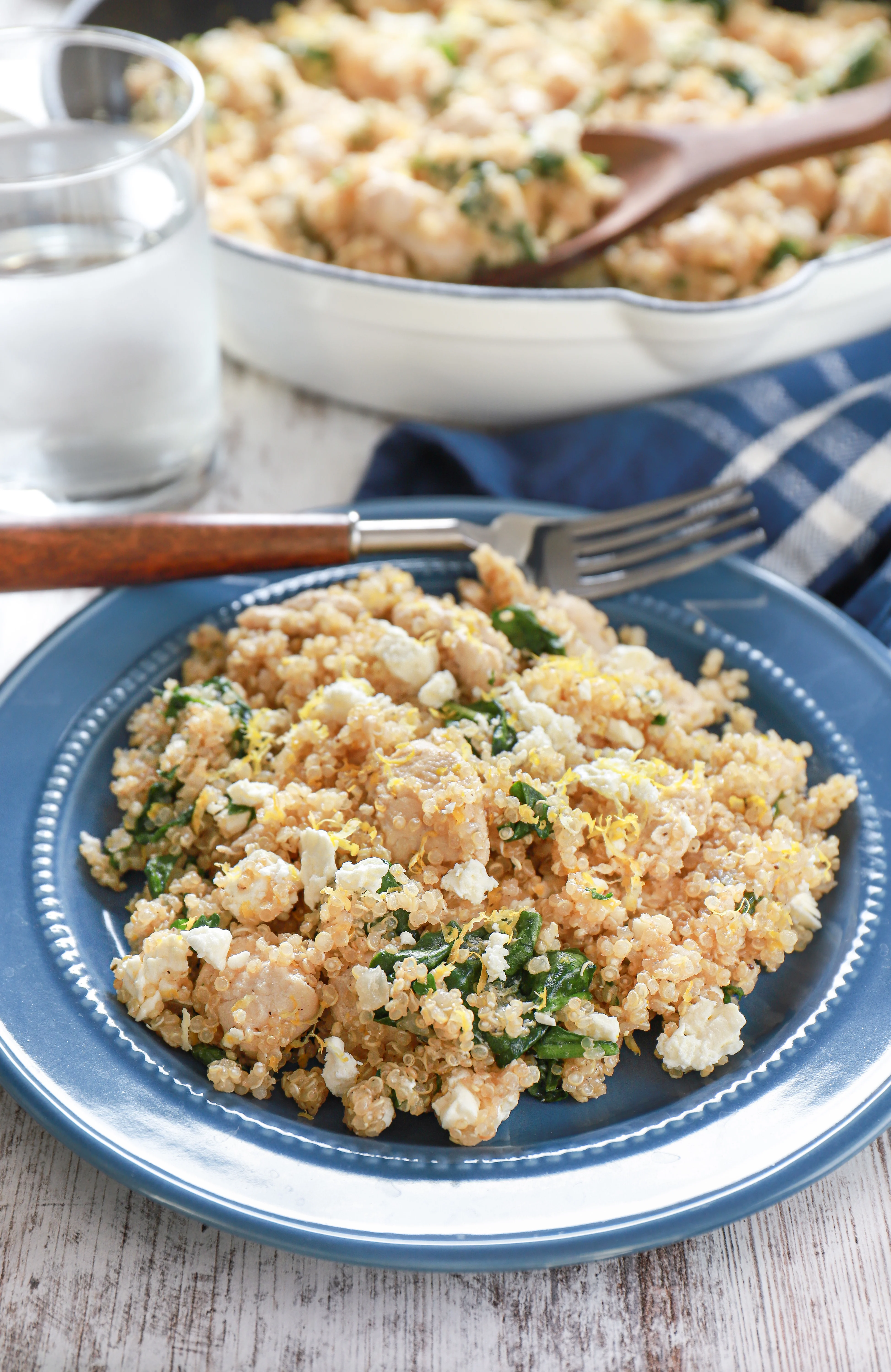 Lemon feta chicken quinoa salad on a blue dinner plate with a white skillet full of quinoa in the background