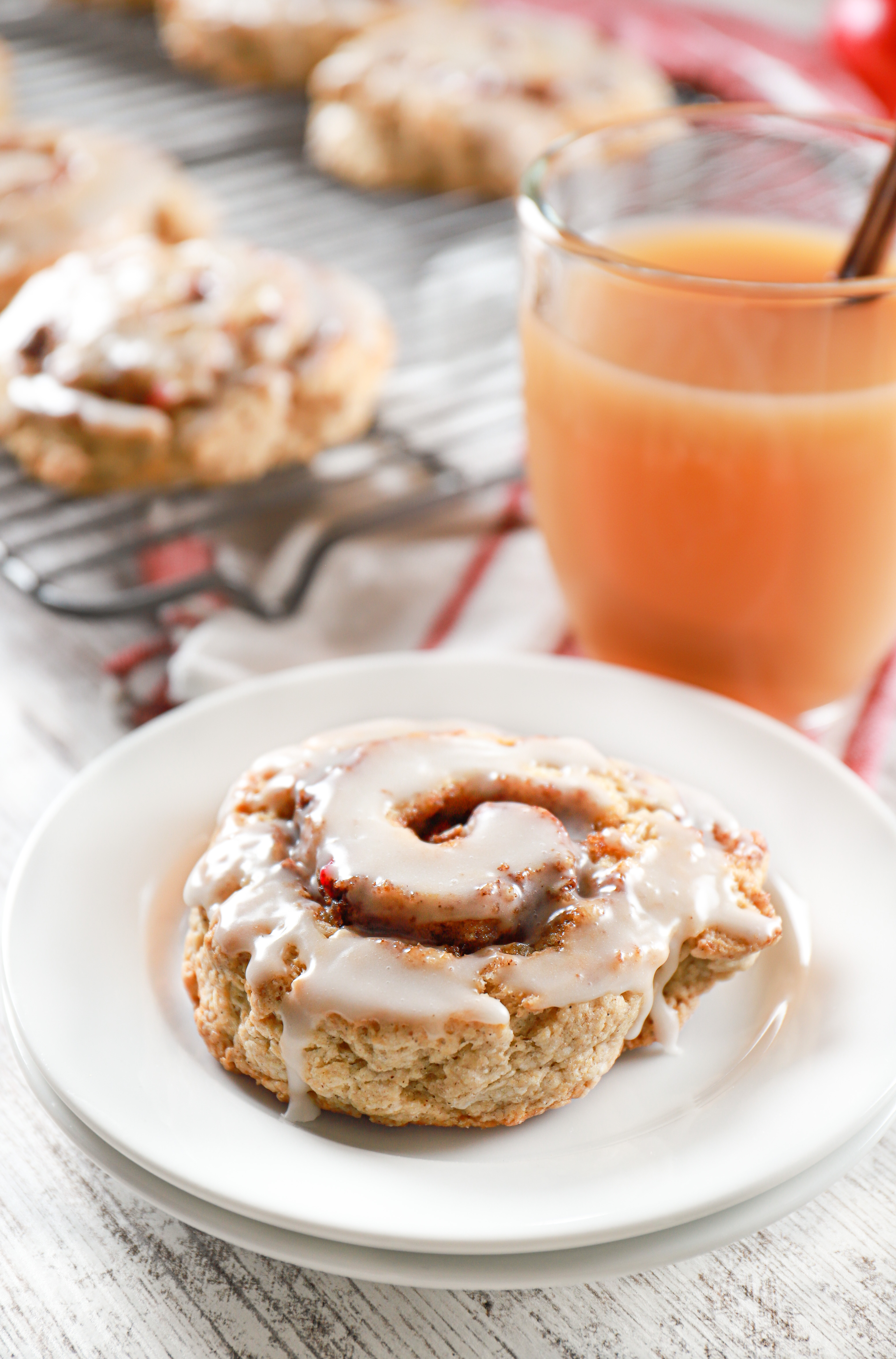 Glazed apple cinnamon roll scone on a small white plate next to a mug of apple cider