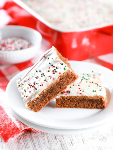 Two glazed gingerbread bars on a small white plate with a red baking dish in the background.