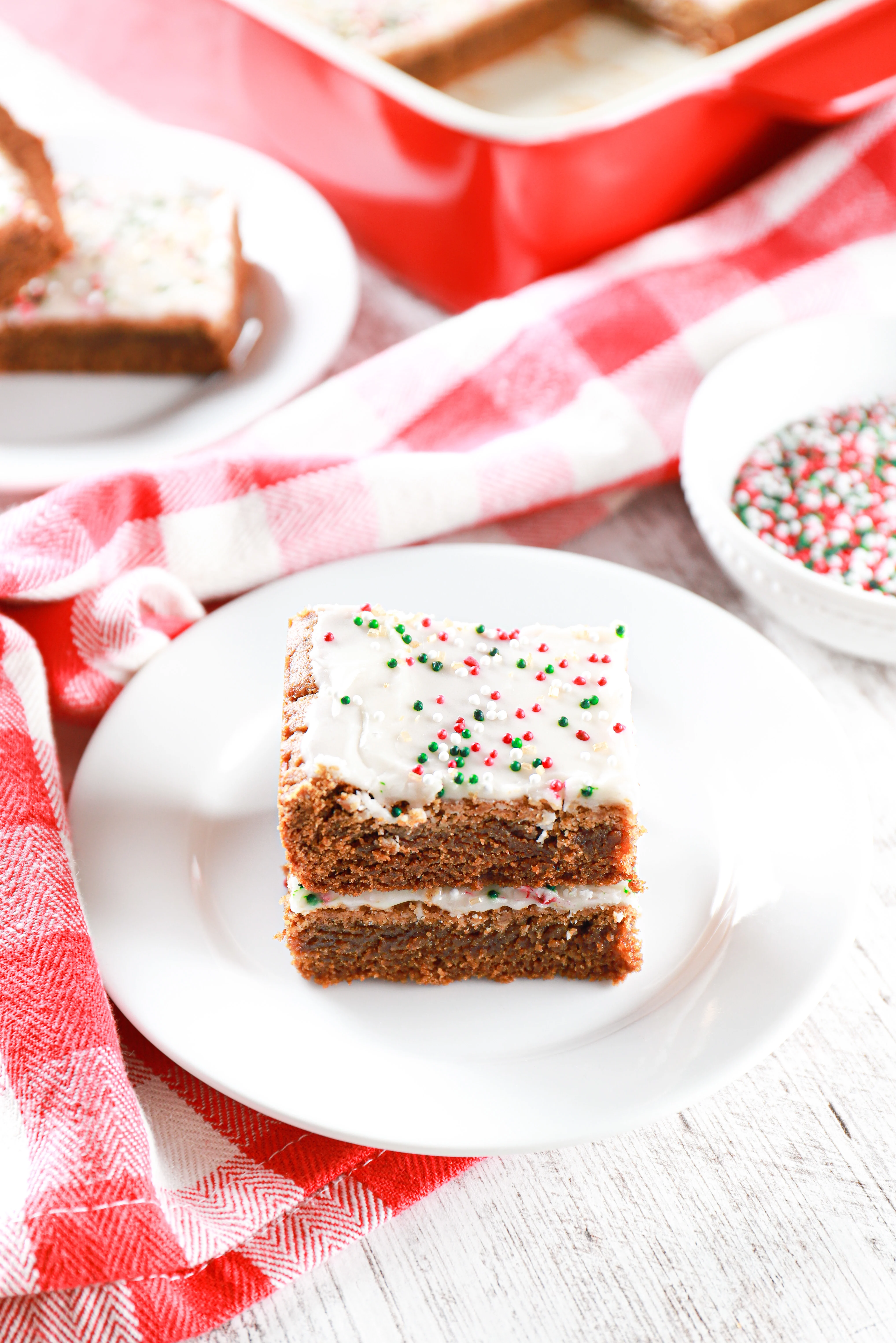 Two soft baked gingerbread bars stacked on a small white plate with a red checked towel curved around the plate. 