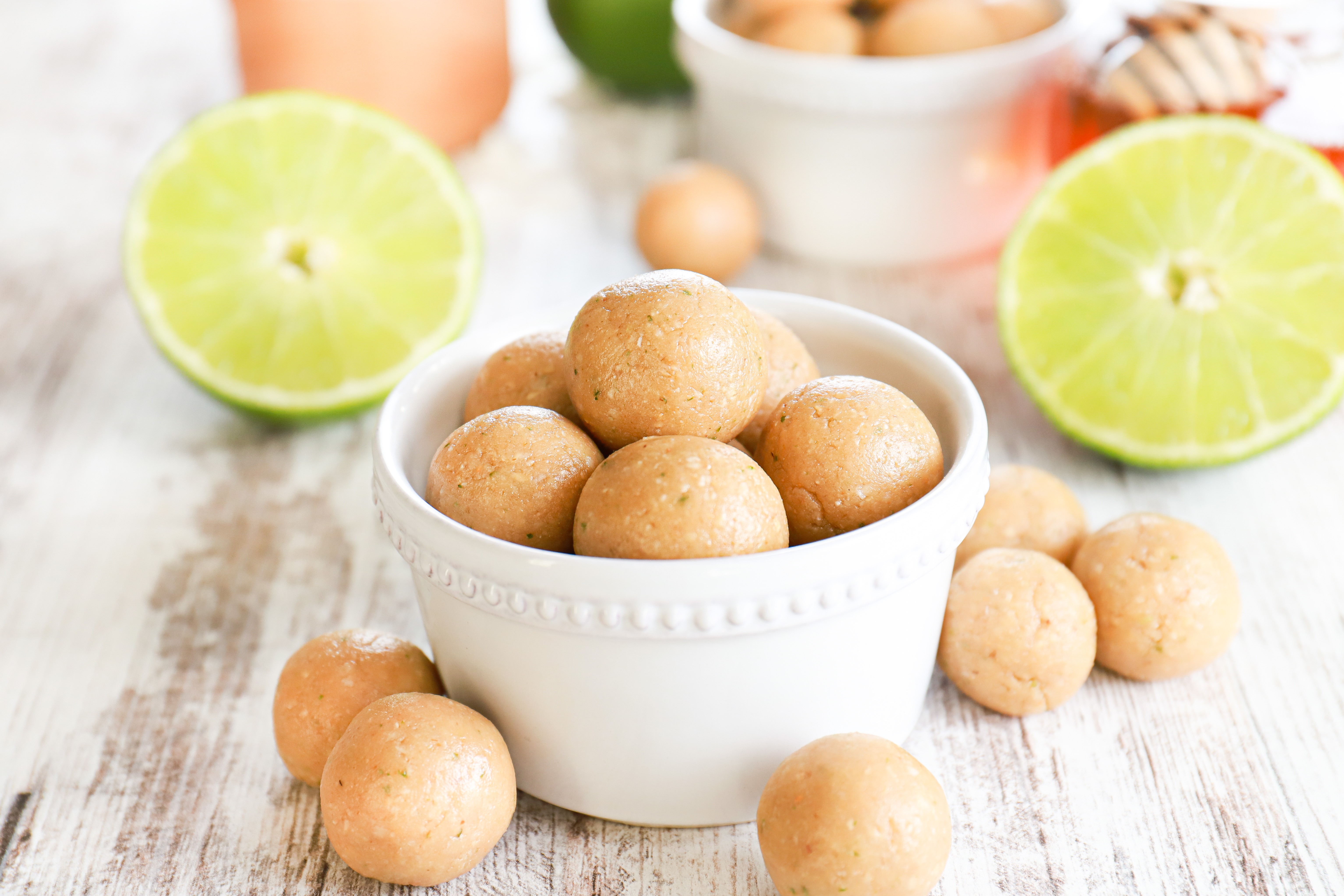 Coconut lime protein balls in a small white dish with coconut and lime halves in the background.