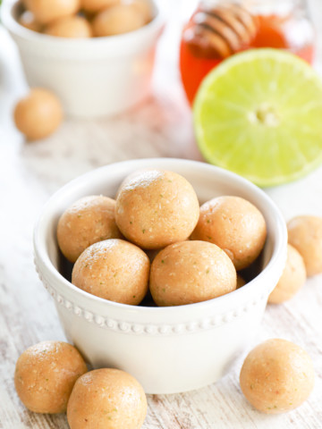 Coconut lime protein bites in a small white bowl with a half lime and jar of honey in the background.