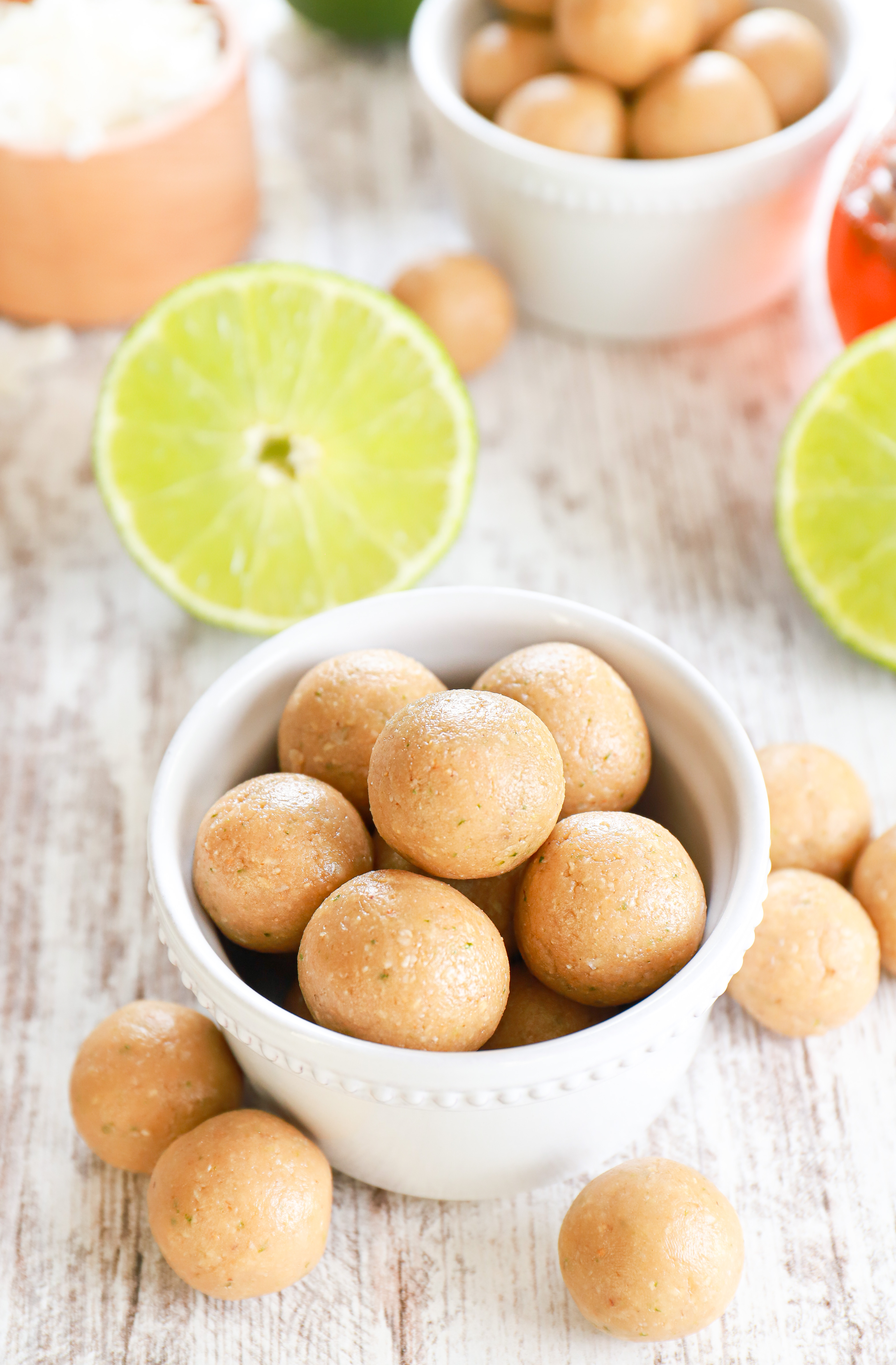 Above view of two small white bowls full of coconut lime protein bites surrounded by lime halves and a jar of honey.