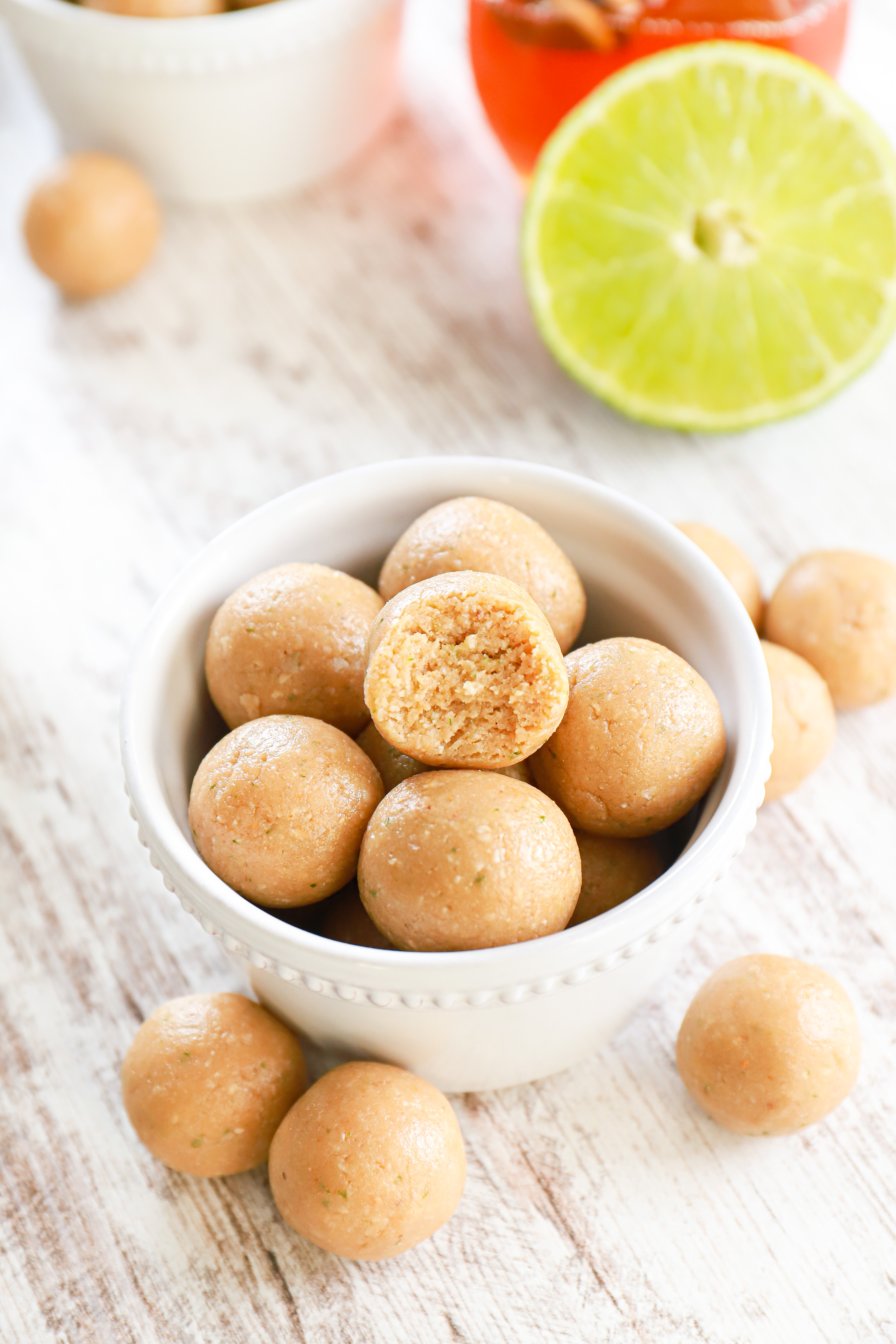 Small white bowl full of coconut lime protein balls with one ball that has a bite taken out of it.