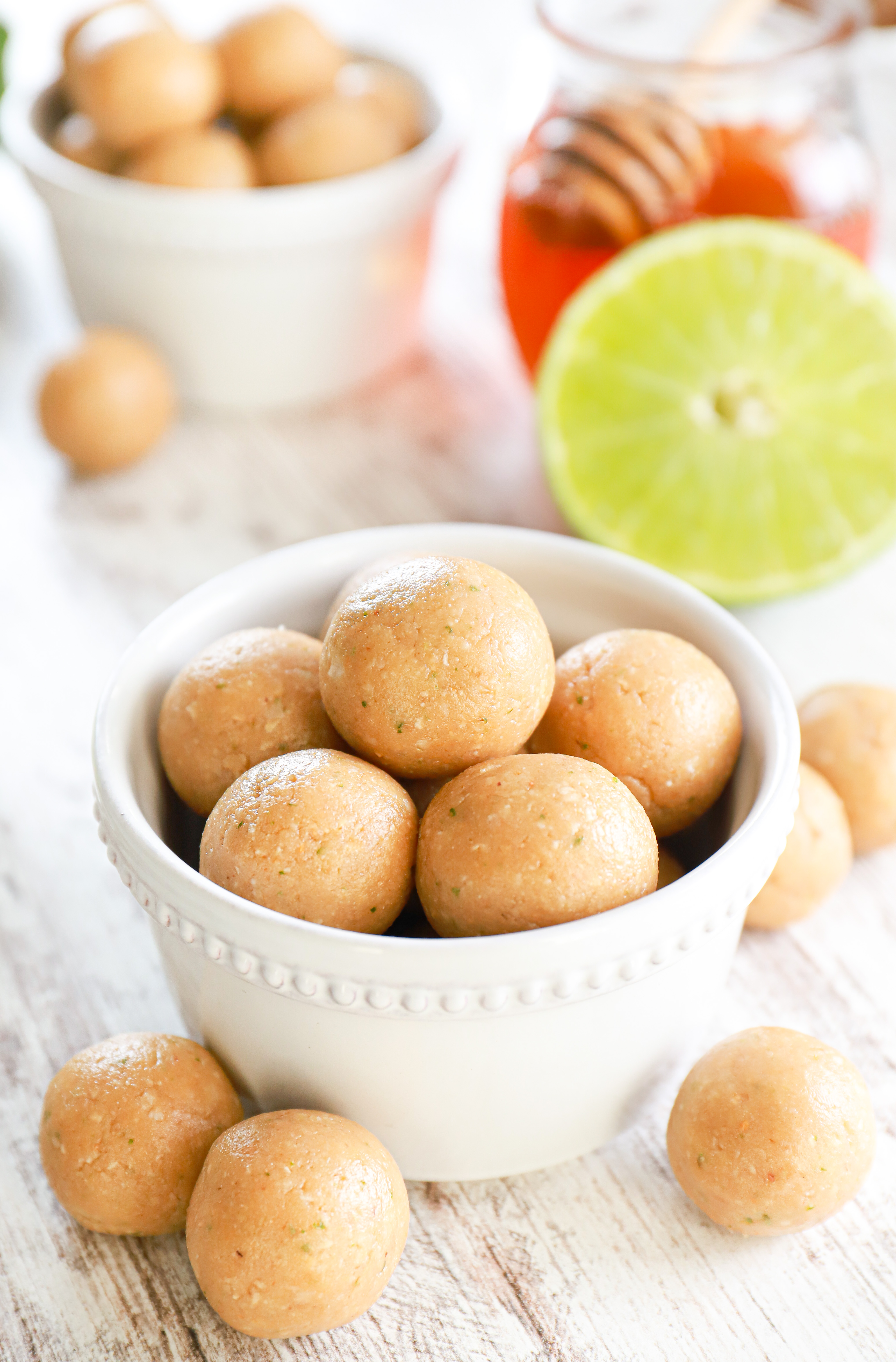 Coconut lime protein bites in a small white bowl with a half lime and jar of honey in the background.