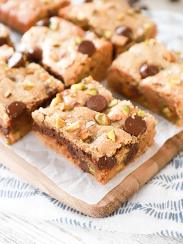 Salted dark chocolate pistachio cookie bars on a parchment paper covered wood cutting board.