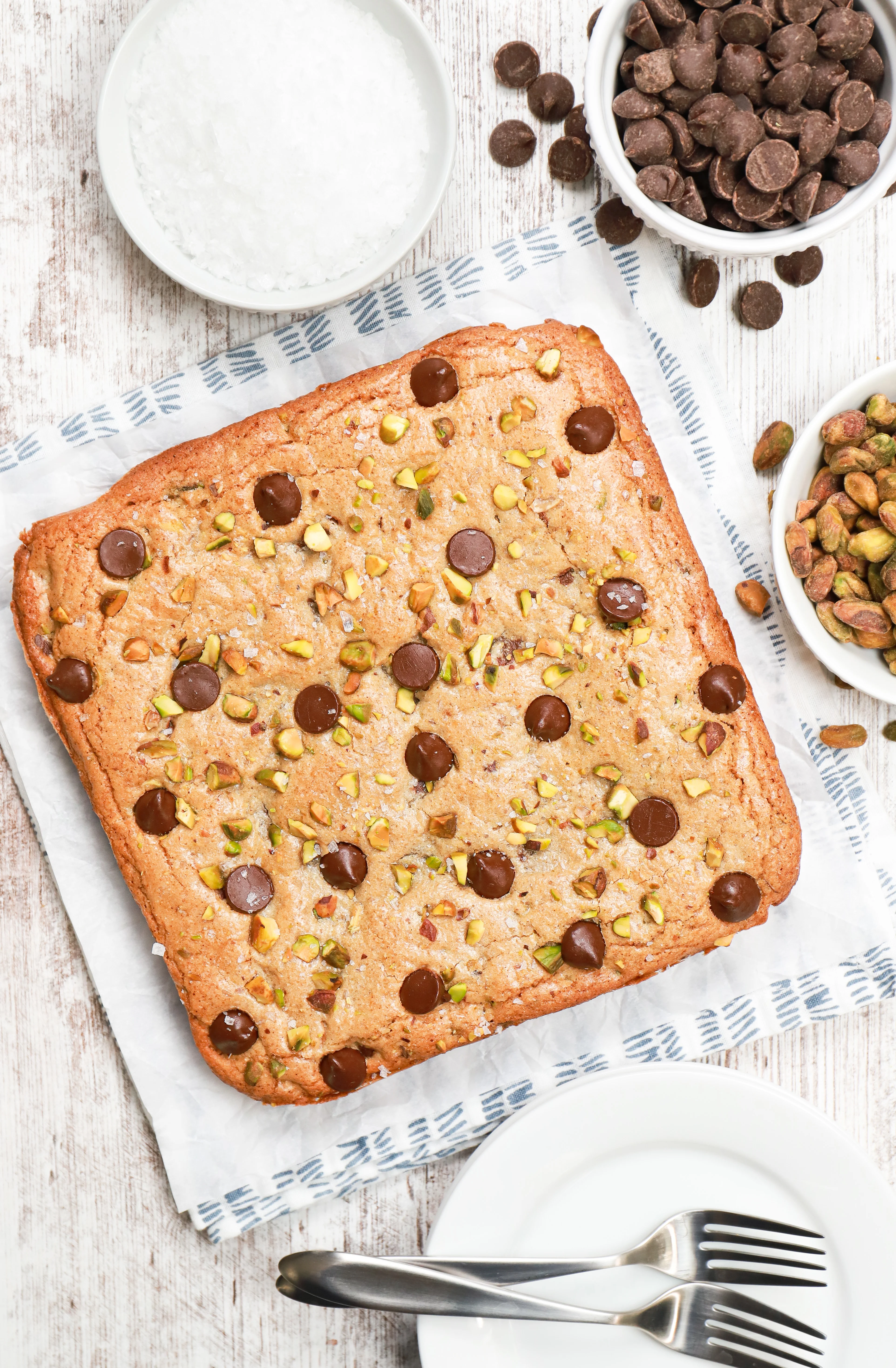 Overhead view of a batch of salted dark chocolate pistachio bars uncut on a piece of parchment paper.