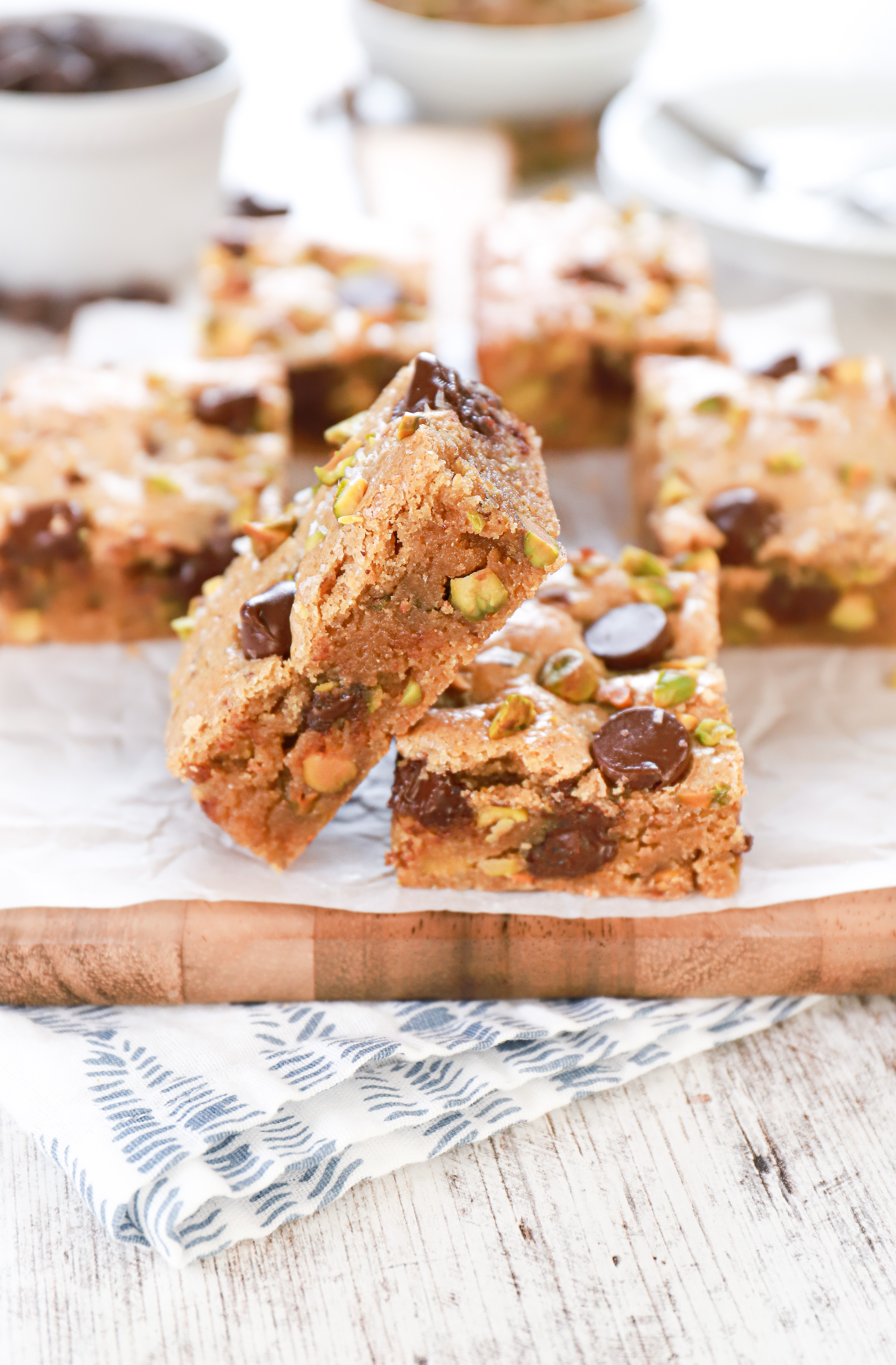 Up close side view of a salted dark chocolate pistachio blondie bar on a parchment paper covered cutting board with more bars in the background.