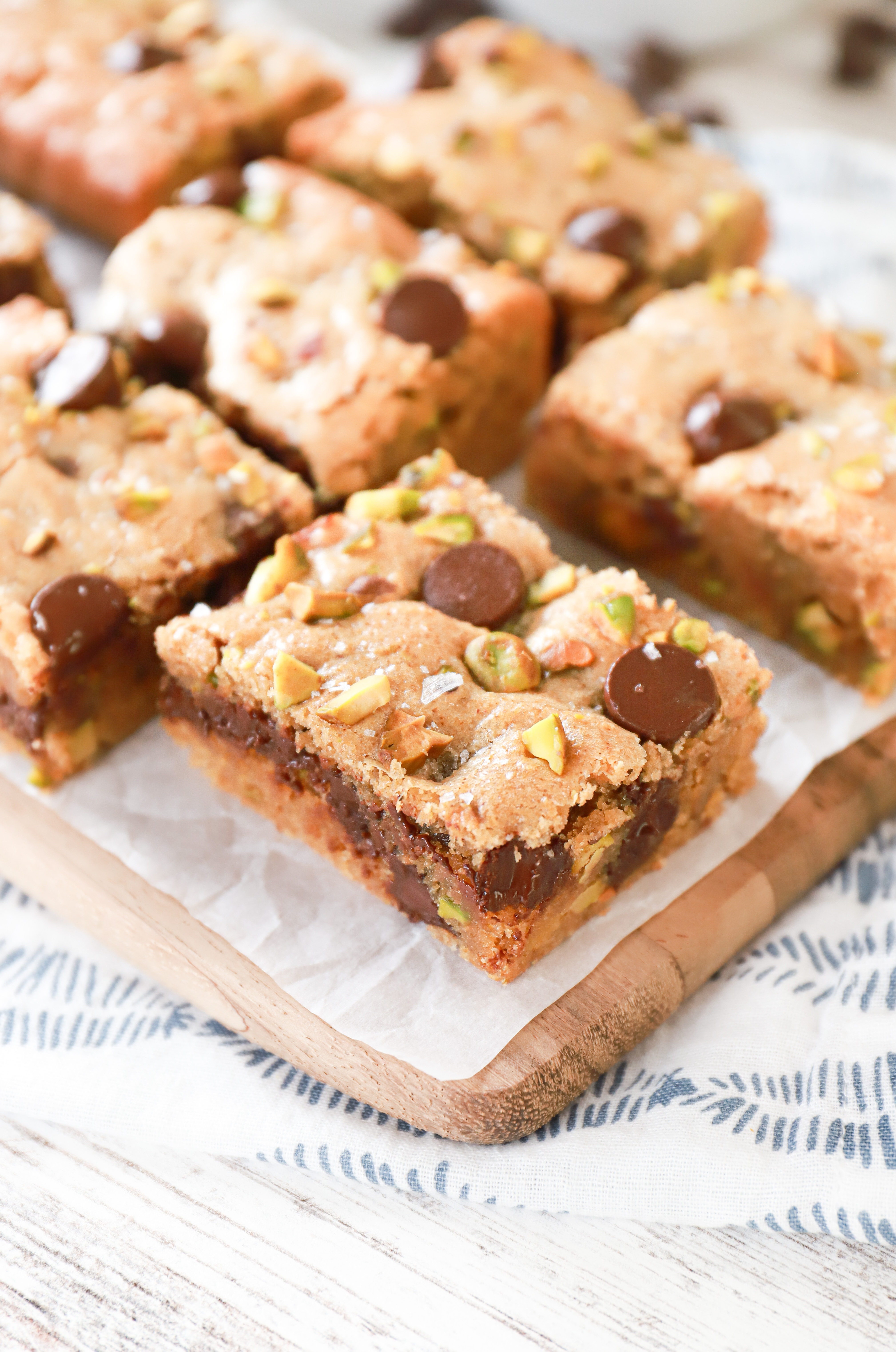 Salted dark chocolate pistachio cookie bars on a parchment paper covered wood cutting board.