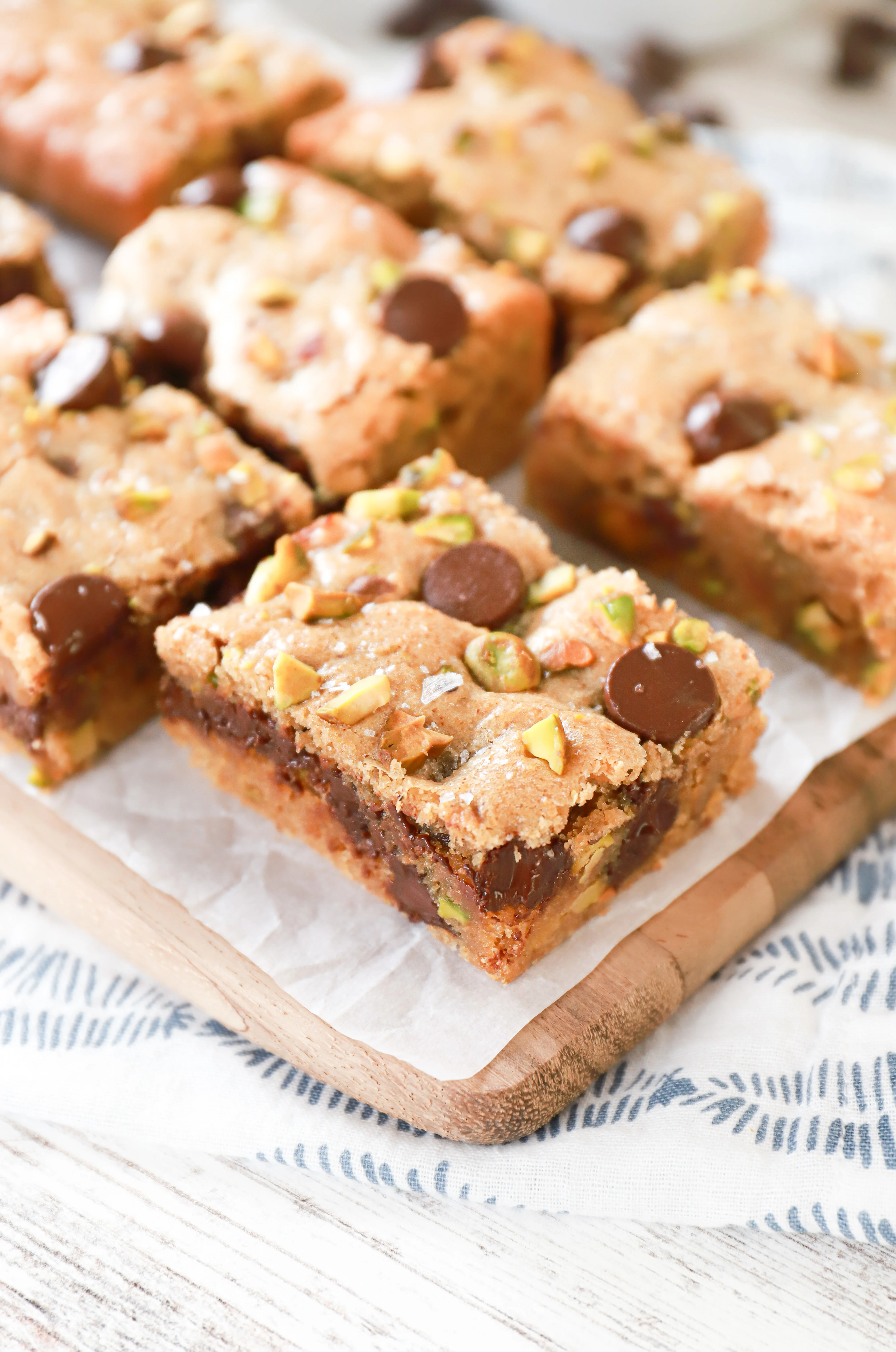 Salted dark chocolate pistachio cookie bars on a parchment paper covered wood cutting board.
