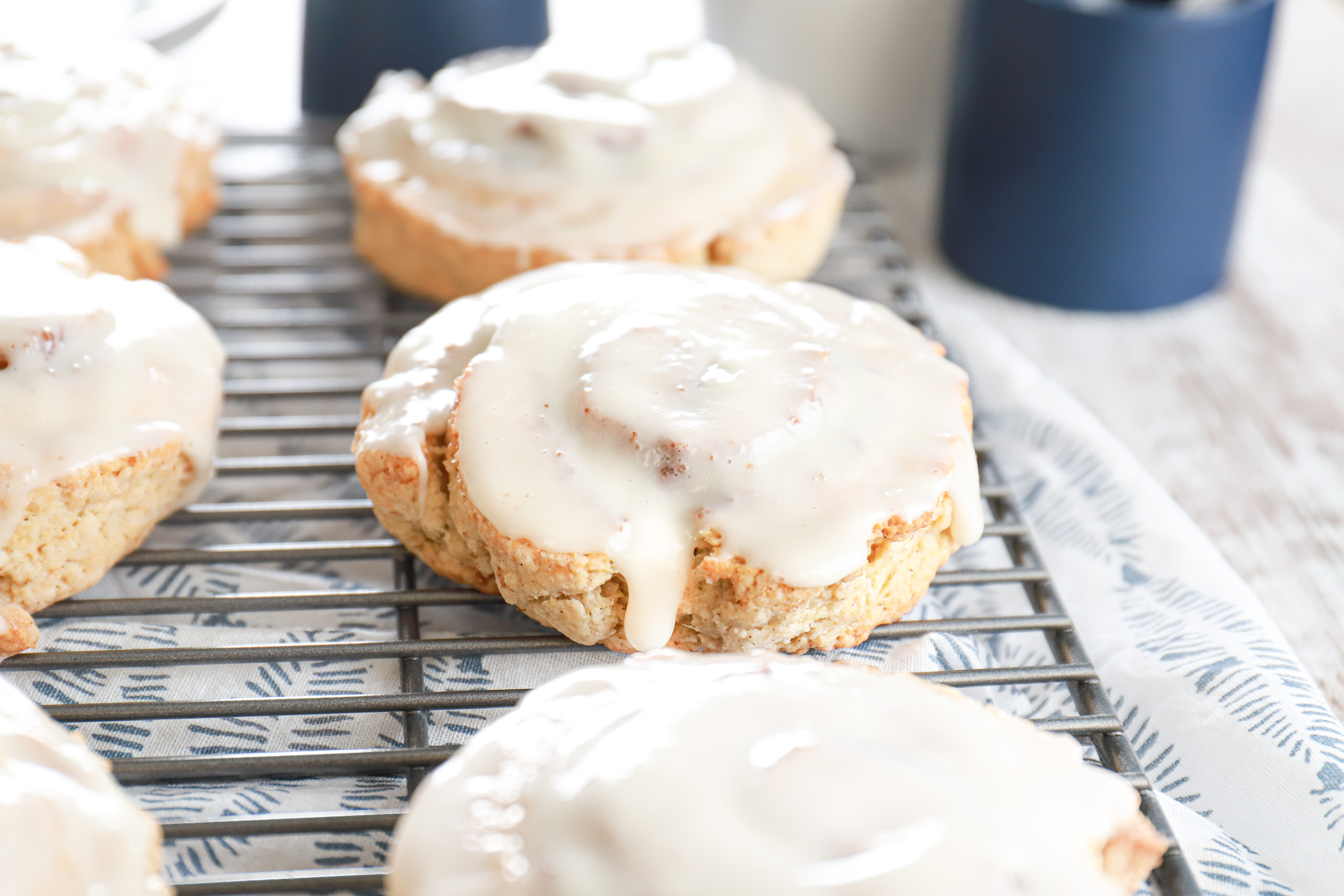 Up close side view of a cinnamon roll scone on a wire cooling rack on top of a white and blue towel.