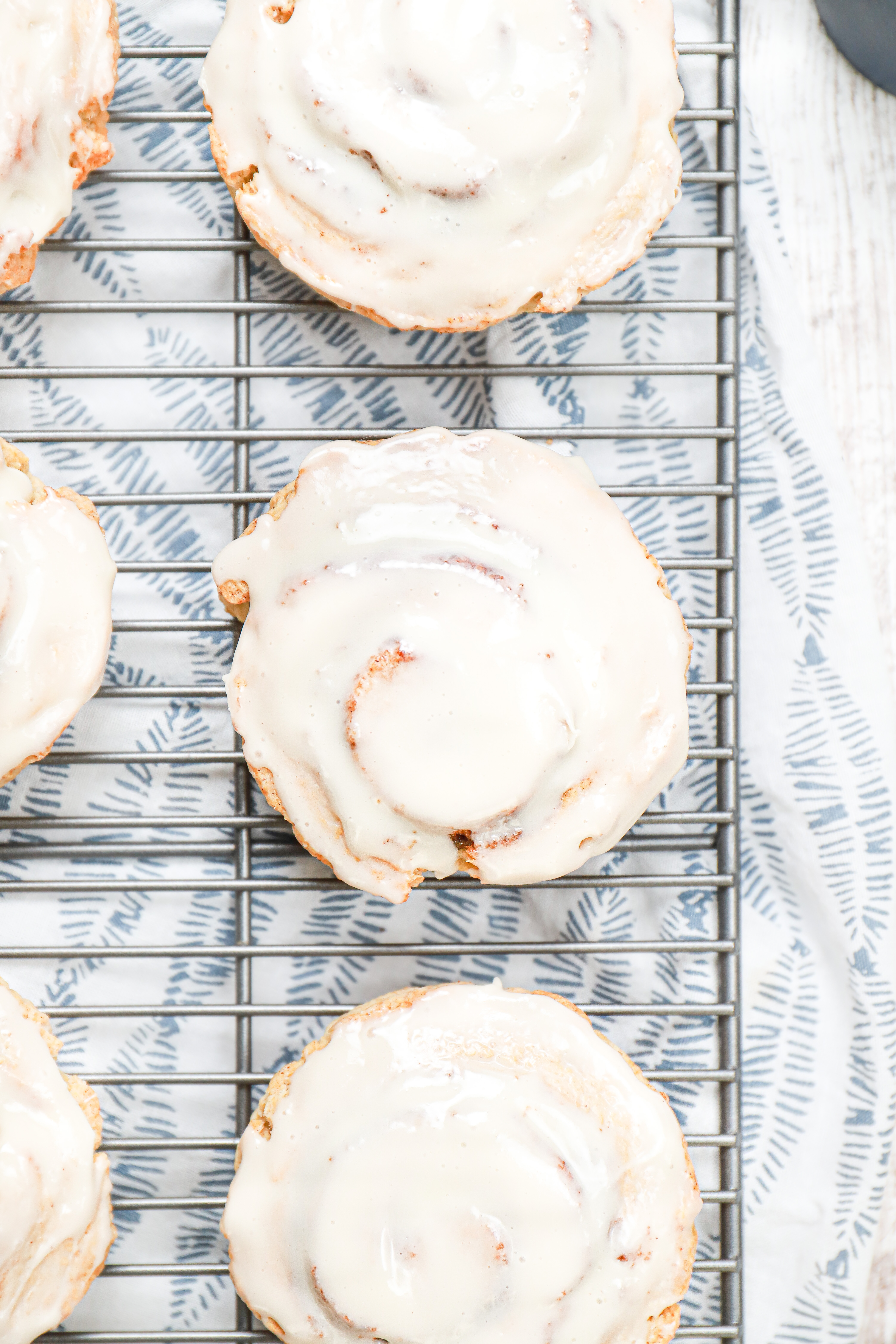 Overhead up close view of a cream cheese glazed cinnamon roll scone on a wire cooling rack on top of a white and blue towel.