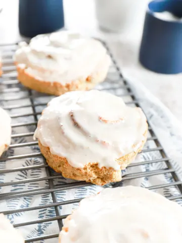 Cinnamon roll scones on a wire cooling rack with blue sugar and cream containers in the background.