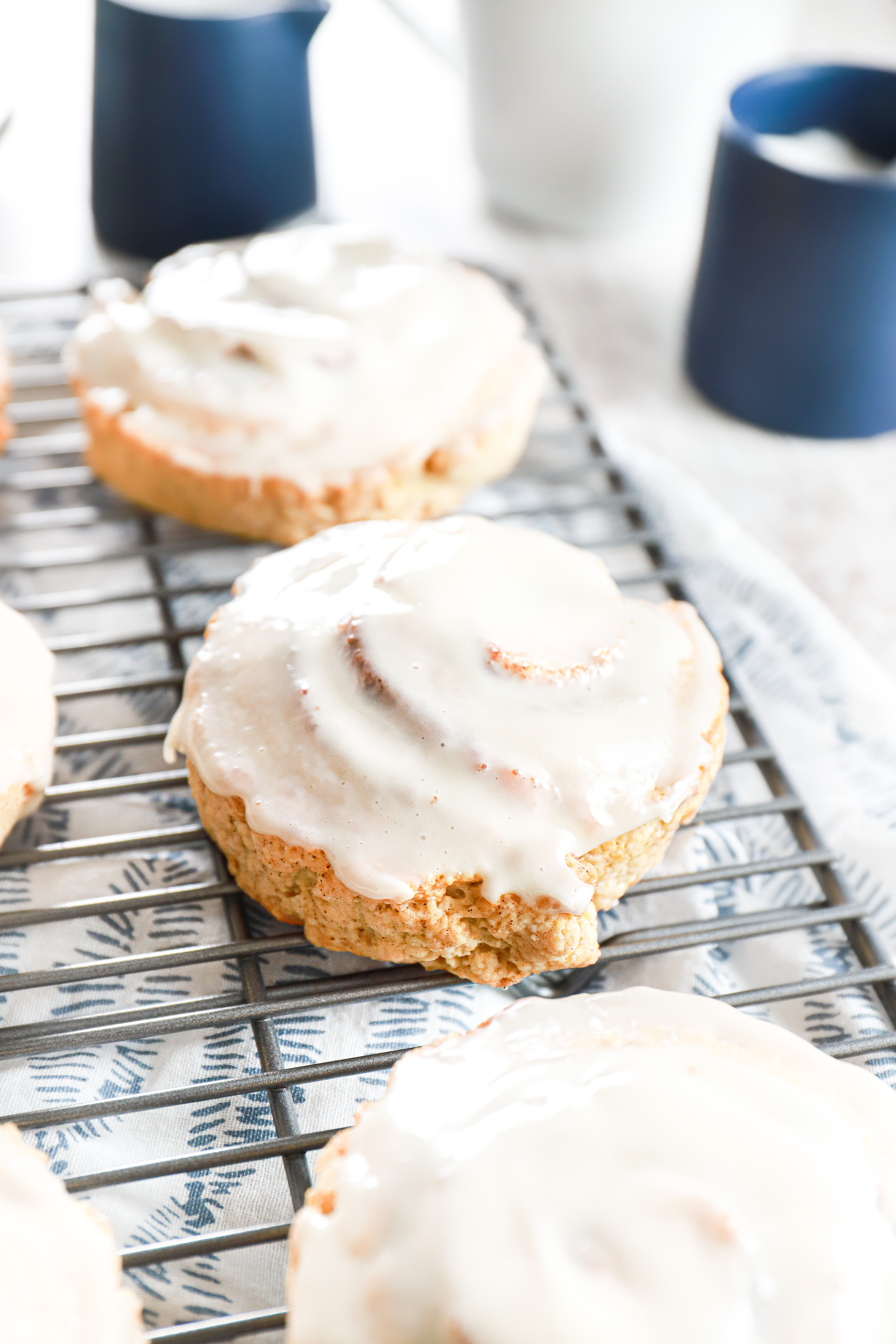 Cinnamon roll scones on a wire cooling rack with blue sugar and cream containers in the background.