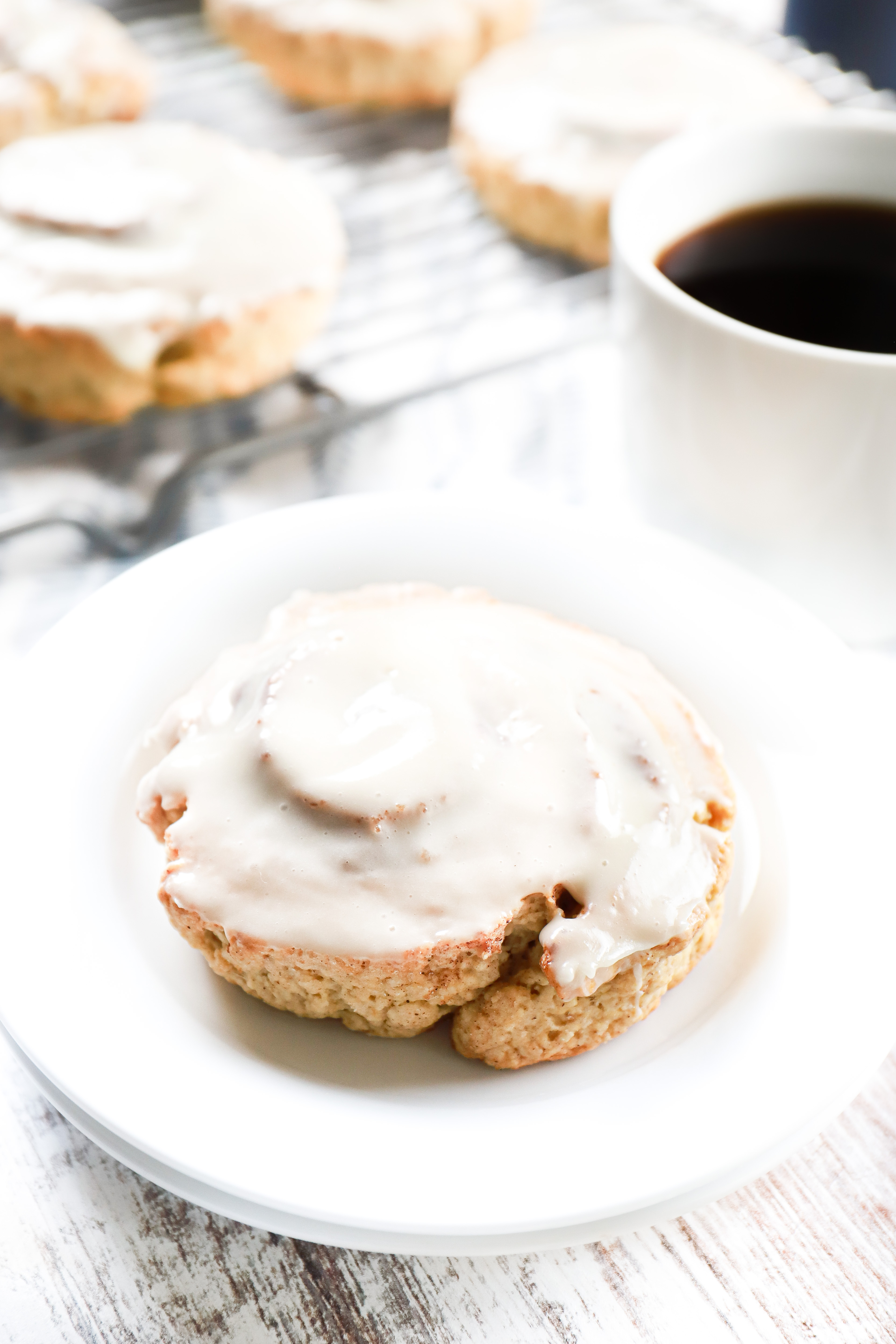 Cinnamon roll scone on a small white plate with more scones on a cooling rack in the background.