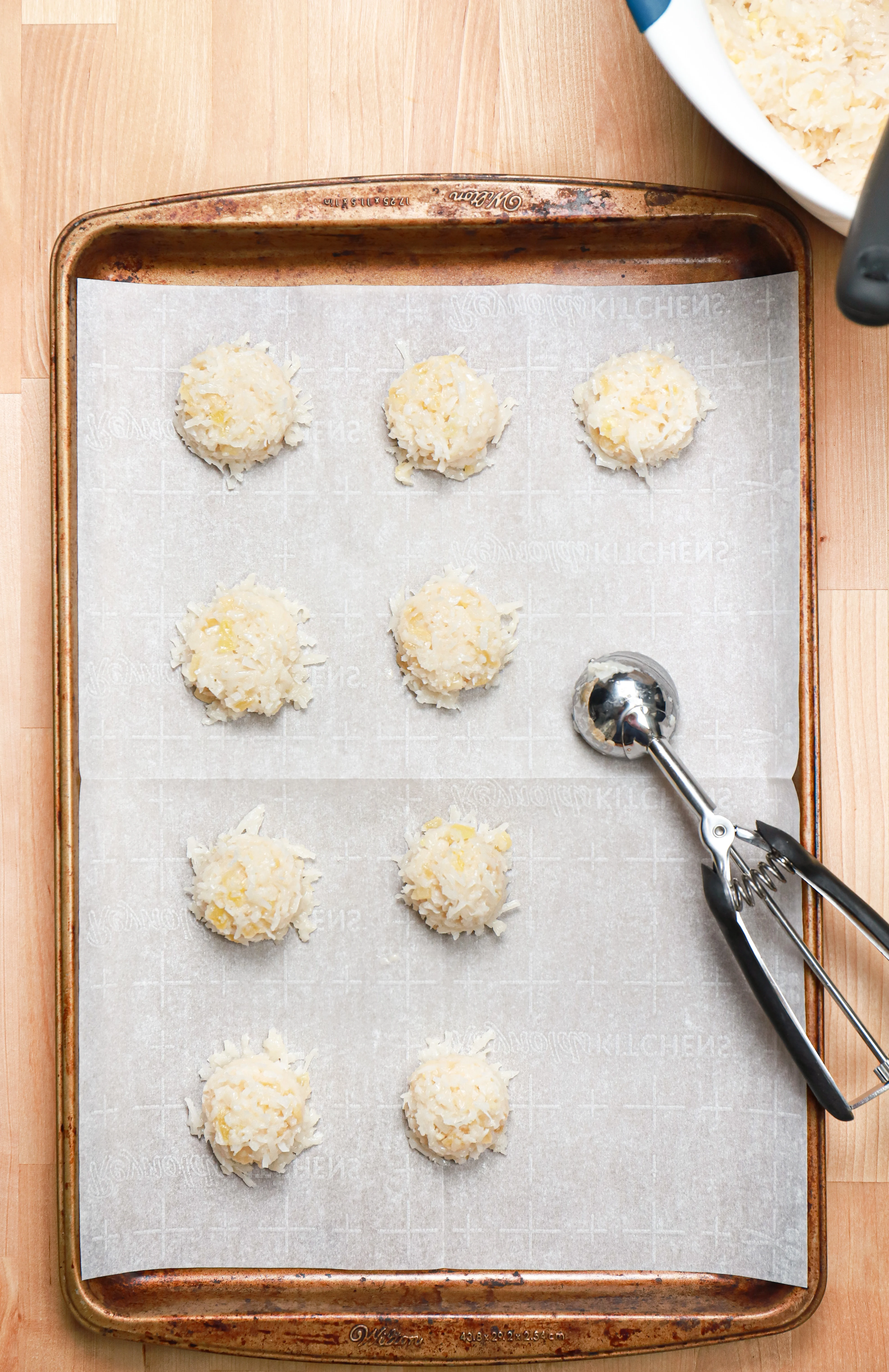 Overhead view of pineapple coconut macaroons on a parchment paper lined baking sheet before being baked.